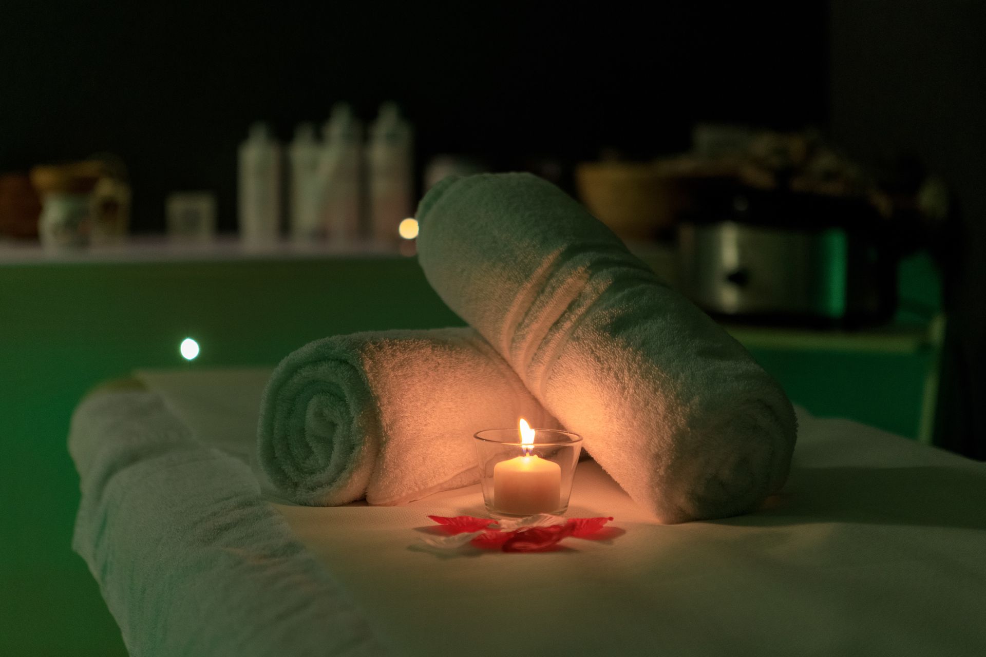 Lettino da trattamento spa con asciugamani bianchi arrotolati, una candela accesa.