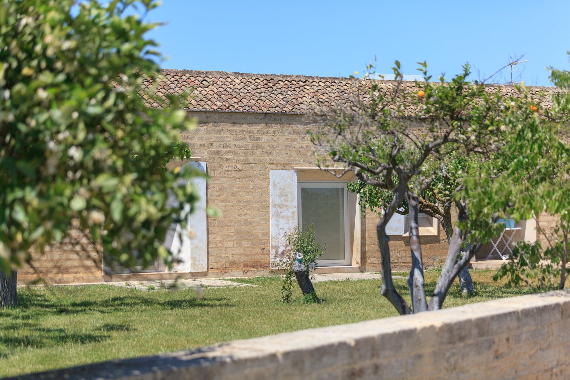 Casa in mattoni con persiane bianche e tetto di tegole, sullo sfondo di un cortile erboso e alberi.