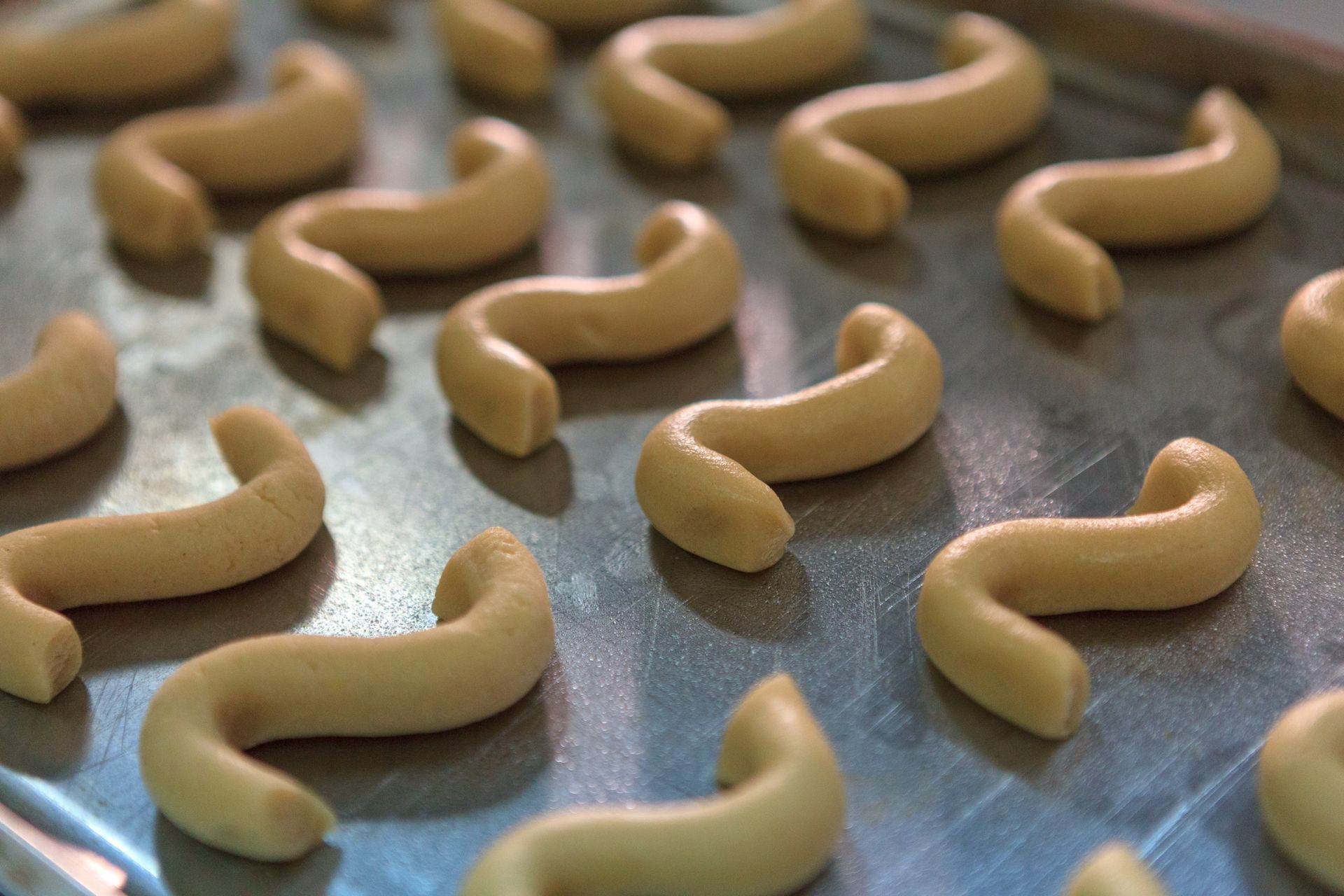 File di biscotti a forma di mezzaluna in cottura su una teglia di metallo