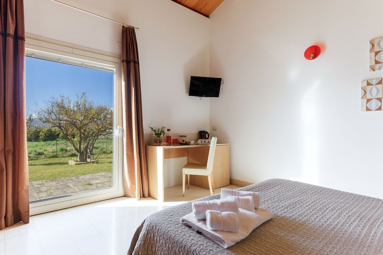 Luminosa camera da letto con letto, scrivania vicino alla finestra, TV a parete e vista sul giardino.