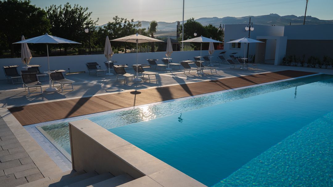 Piscina blu con lettini e ombrelloni accanto a un soleggiato patio del resort.