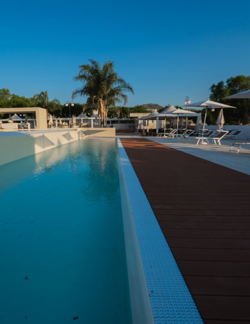 Piscina all'aperto con lettini, ombrelloni e un piccolo edificio sullo sfondo.