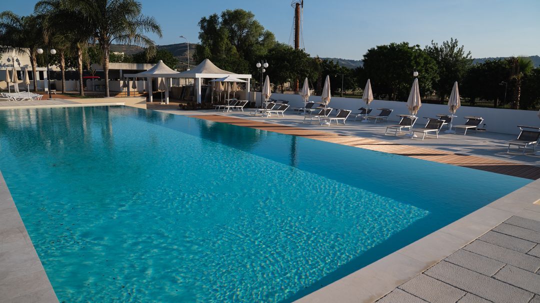 Piscina blu con lettini e ombrelloni accanto a un soleggiato patio del resort.