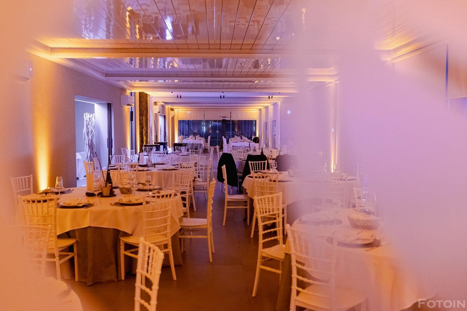 Elegante sala per banchetti con tavoli rotondi, sedie bianche e luci calde.