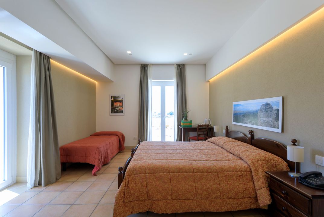 Camera d'albergo moderna con due letti, pareti beige e porta finestra che dà sul balcone.