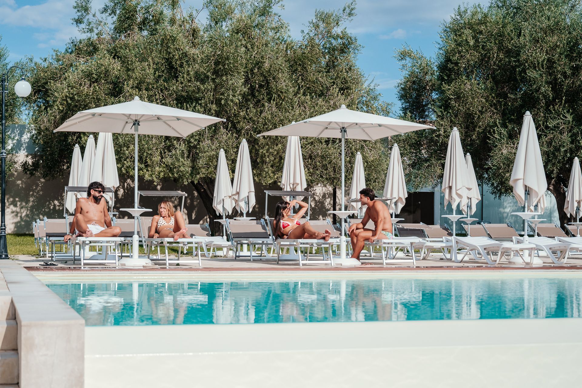 Piscina coperta con ampie vetrate, terrazza in legno e lettini prendisole con vista sull'acqua.