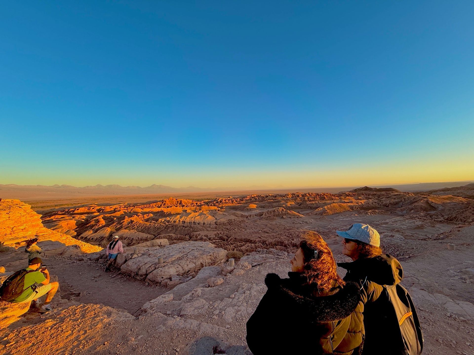 Dos excursionistas contemplan un desierto rocoso al atardecer bajo un cielo azul despejado.
