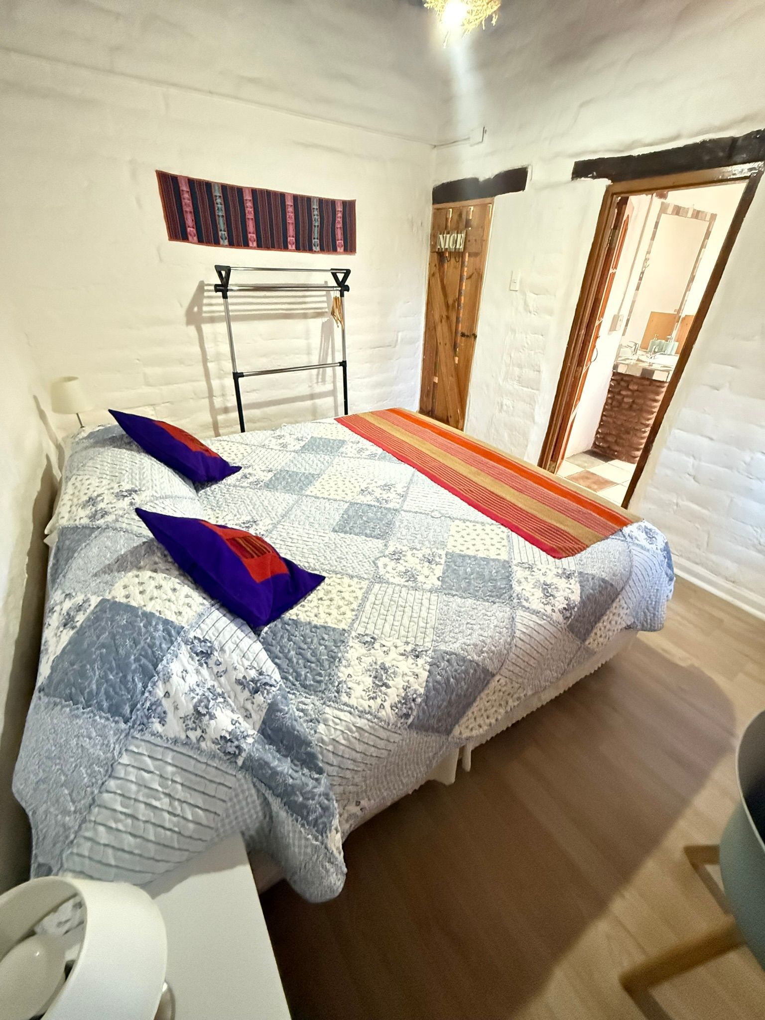 Acogedora habitación con cama, edredón estampado, almohadas coloridas y muebles de madera junto a una ventana luminosa.