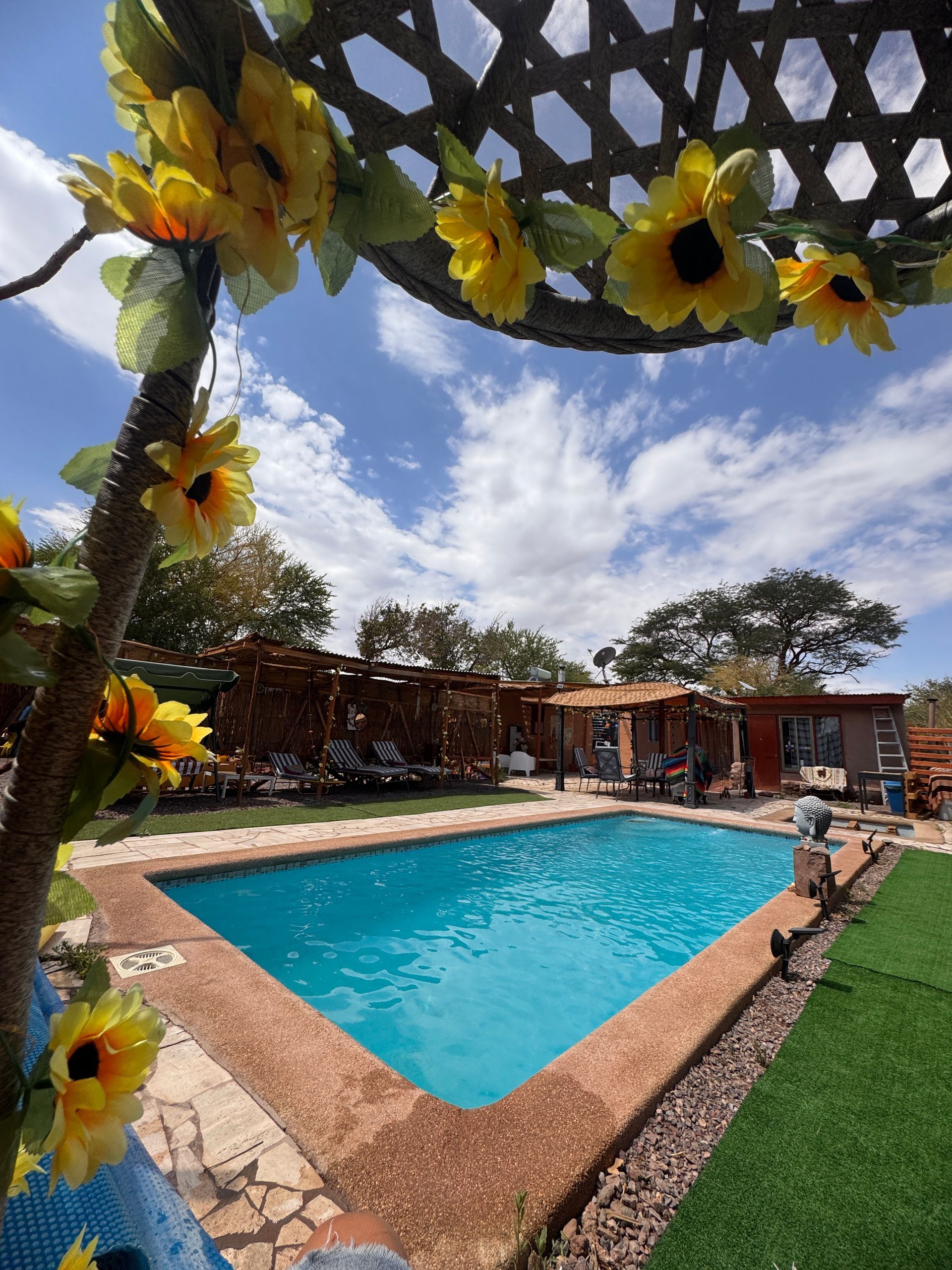 Patio decorado junto a la piscina con una piscina de color turquesa bajo un cielo parcialmente nublado.