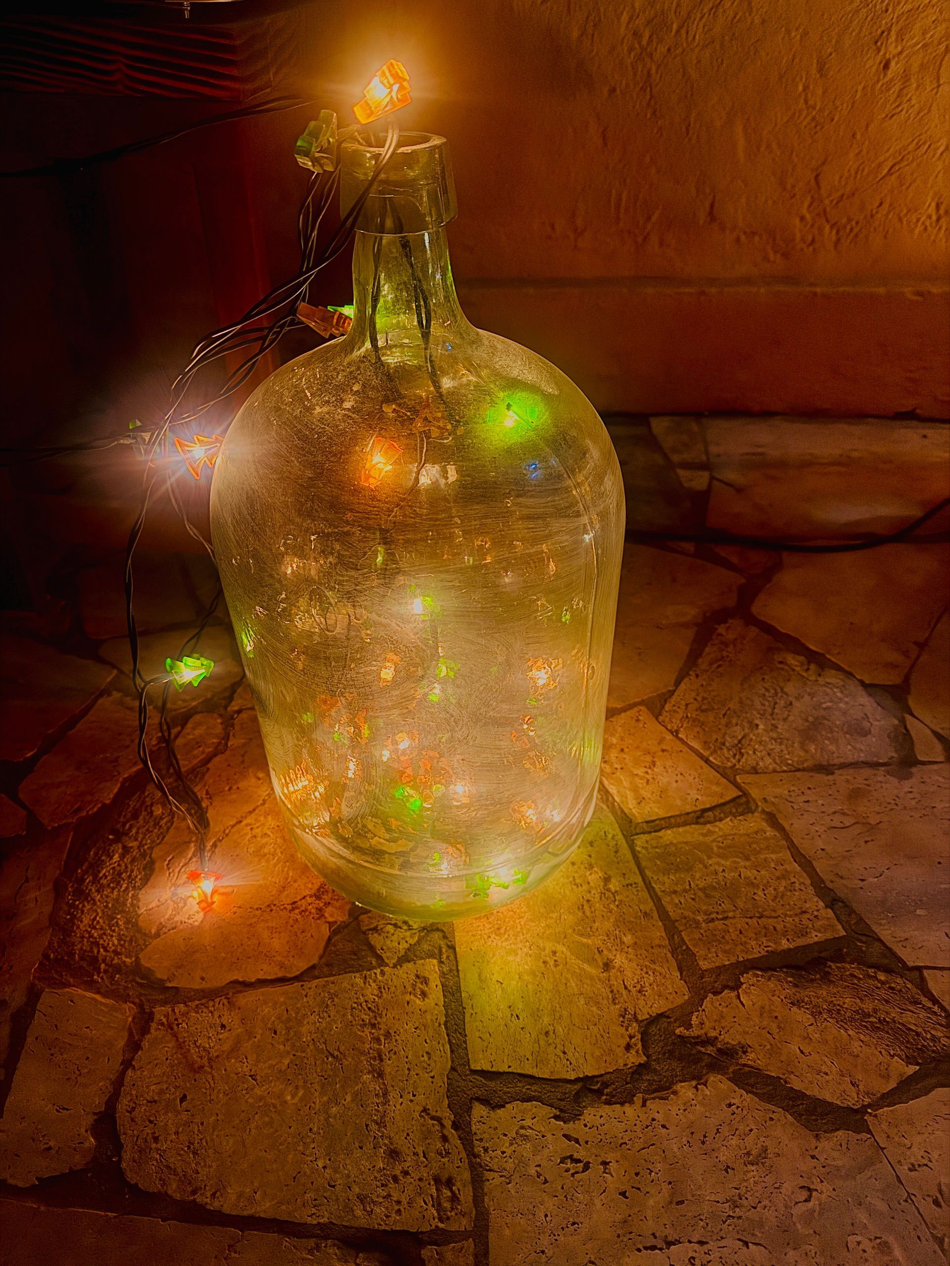 Botella de vidrio brillante con luces de colores en su interior, iluminada por una llama sobre un suelo de piedra.