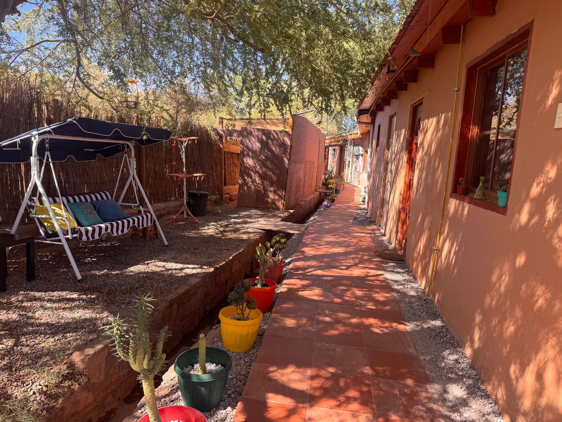 Sendero ajardinado junto a una casa, con macetas, una hamaca y largas sombras bajo la cálida luz del sol.