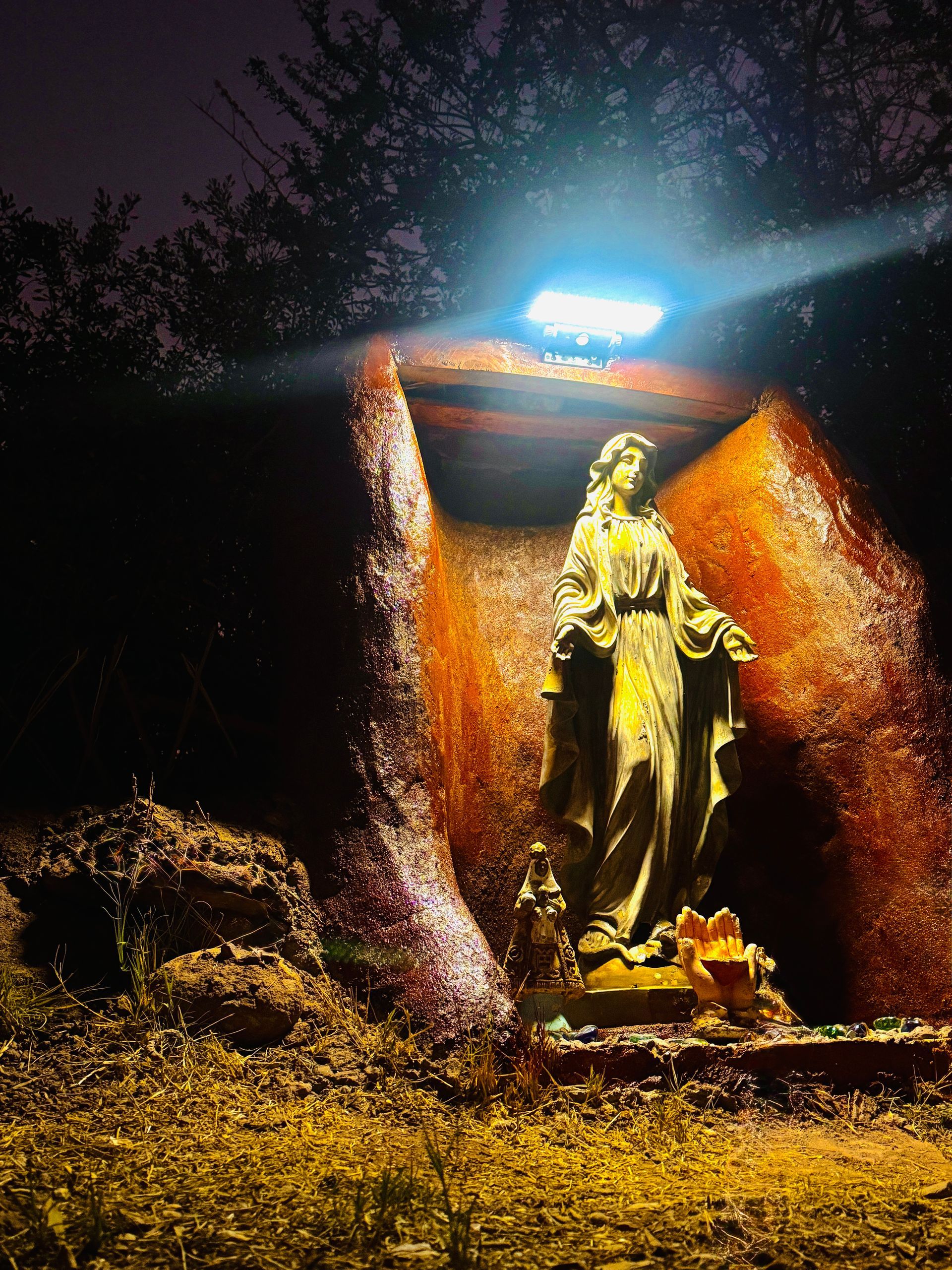 Estatua iluminada con luces azules y naranjas brillantes por la noche, con una pequeña fuente a su lado.