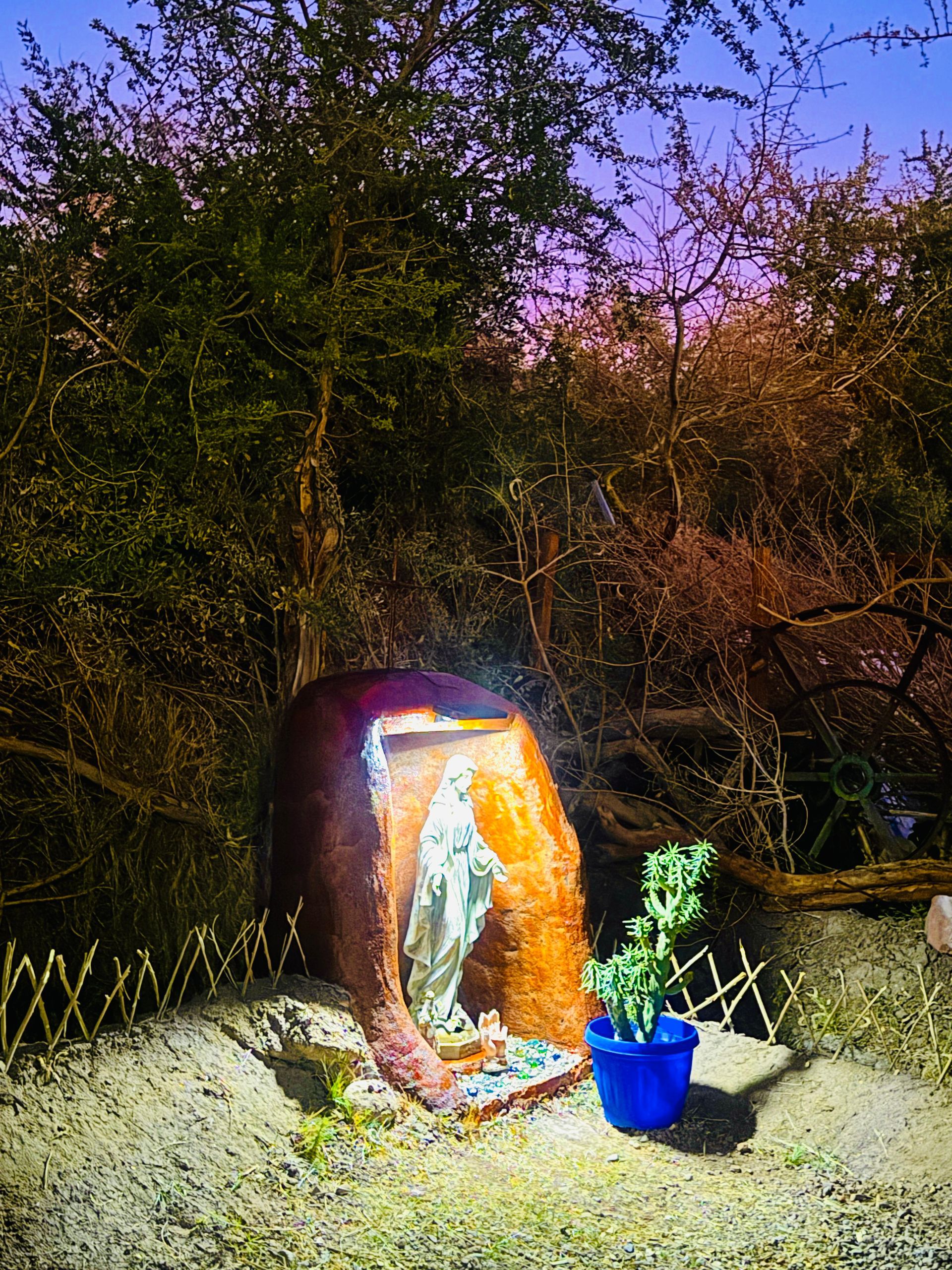 Una fuente de agua resplandeciente al aire libre, junto a una planta azul en maceta, en un jardín al atardecer.