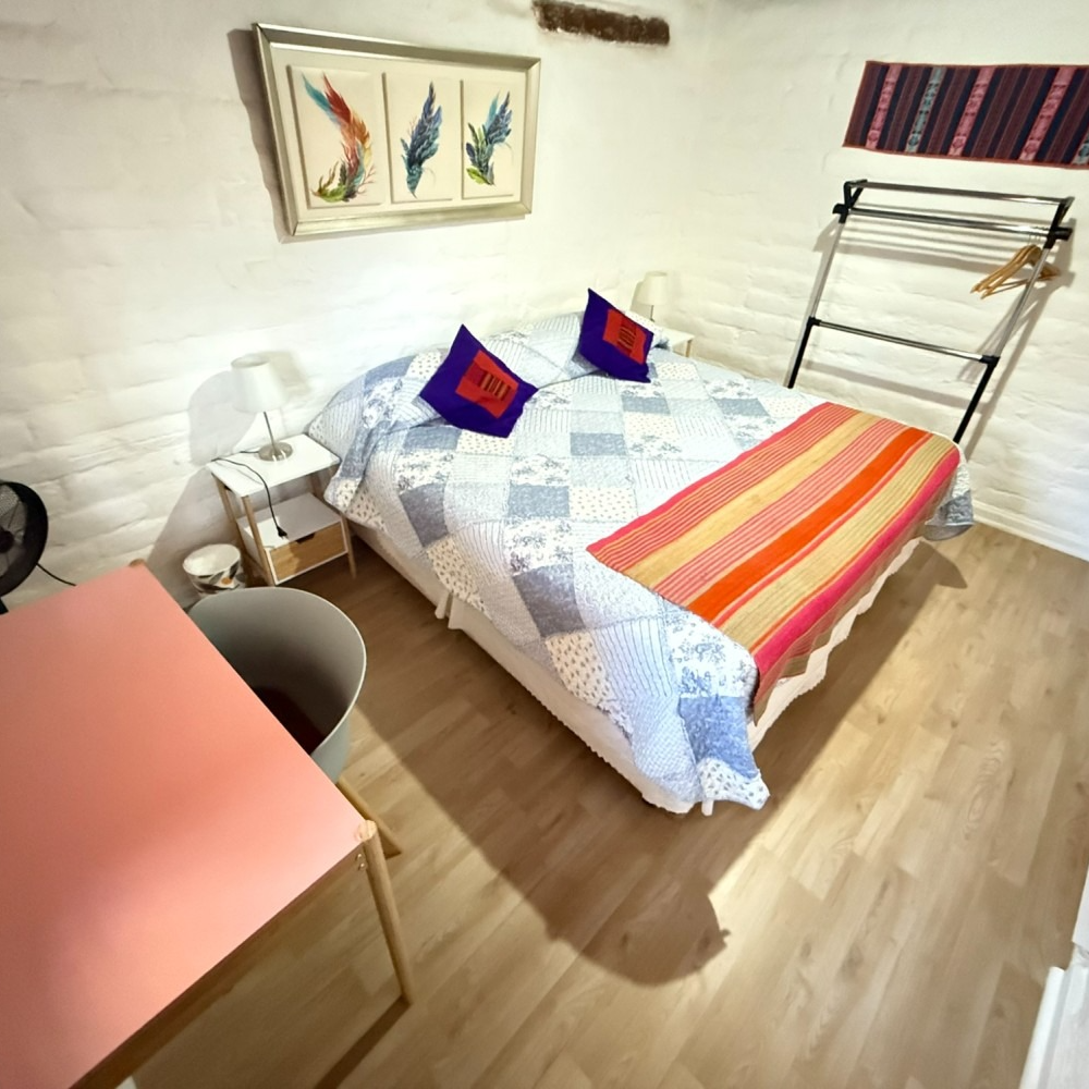 Habitación acogedora con cama baja, manta a rayas, cuadro y paredes de ladrillo blanco.