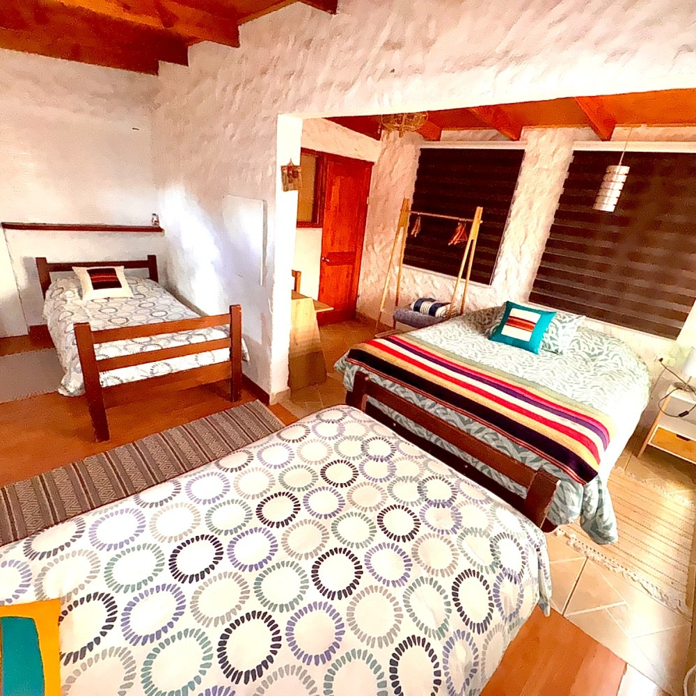 Acogedora habitación con dos camas de madera, colchas estampadas, paredes blancas y cálidas vigas de madera en el techo.