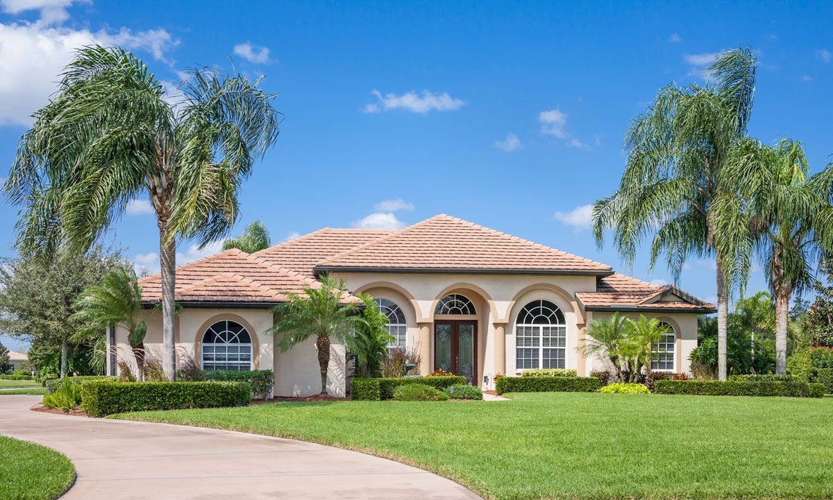 A large house with a driveway and palm trees in front of it.