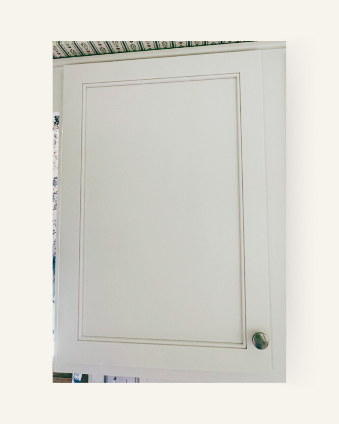 Cream-colored cabinet door with a framed center panel and a round knob.