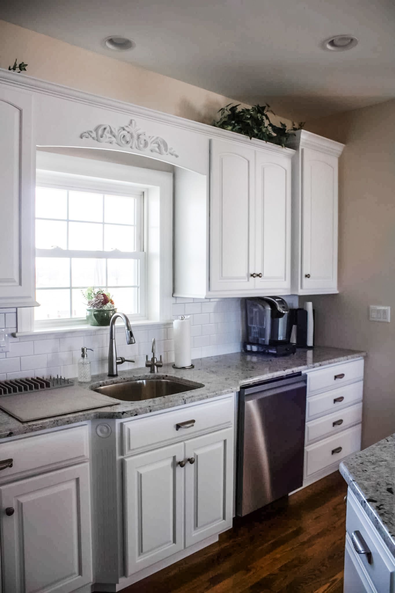 White kitchen cabinets with a window, sink, and stainless steel appliances.