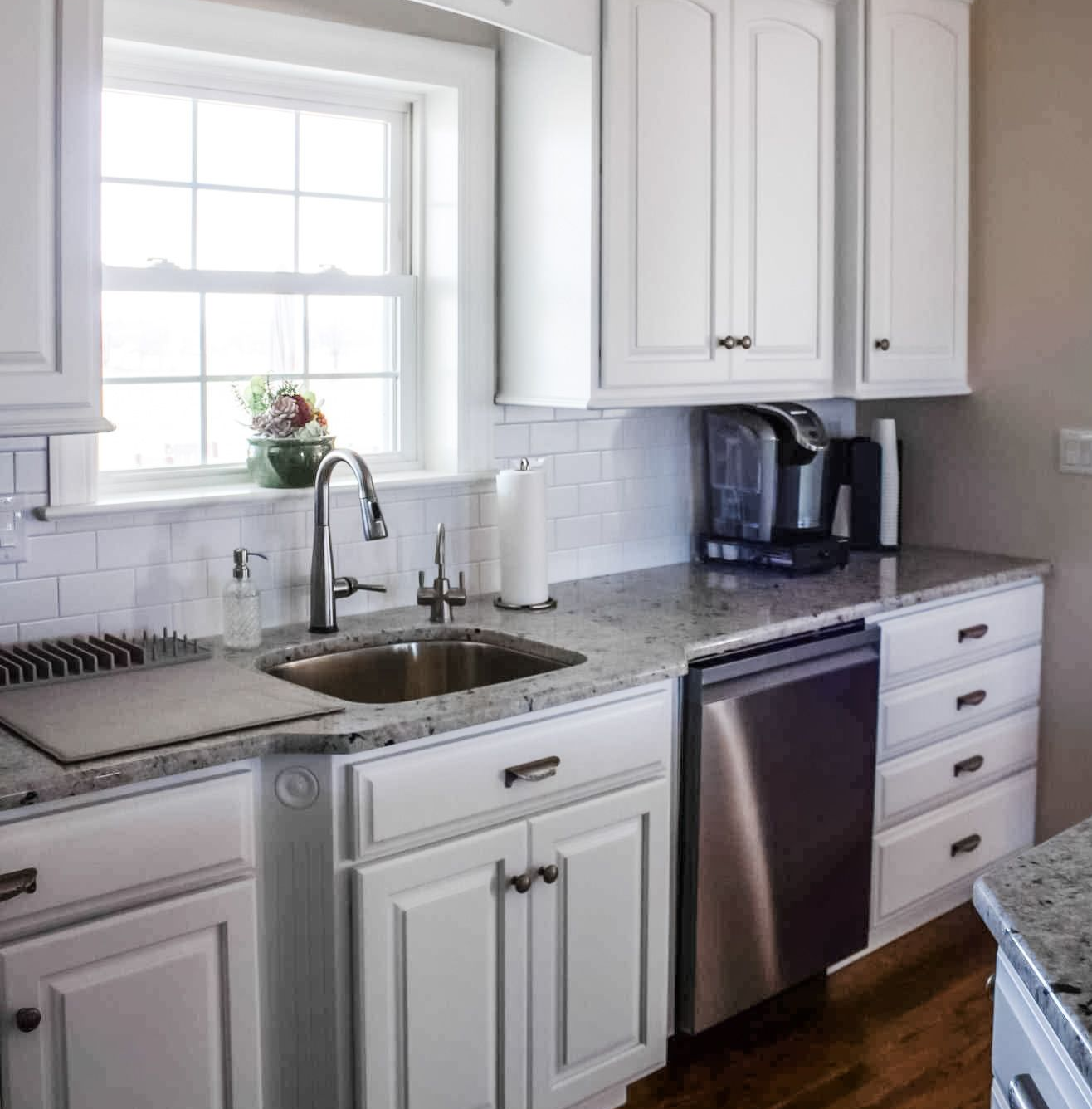 White kitchen with stainless steel appliances, granite countertops, and a window above the sink.