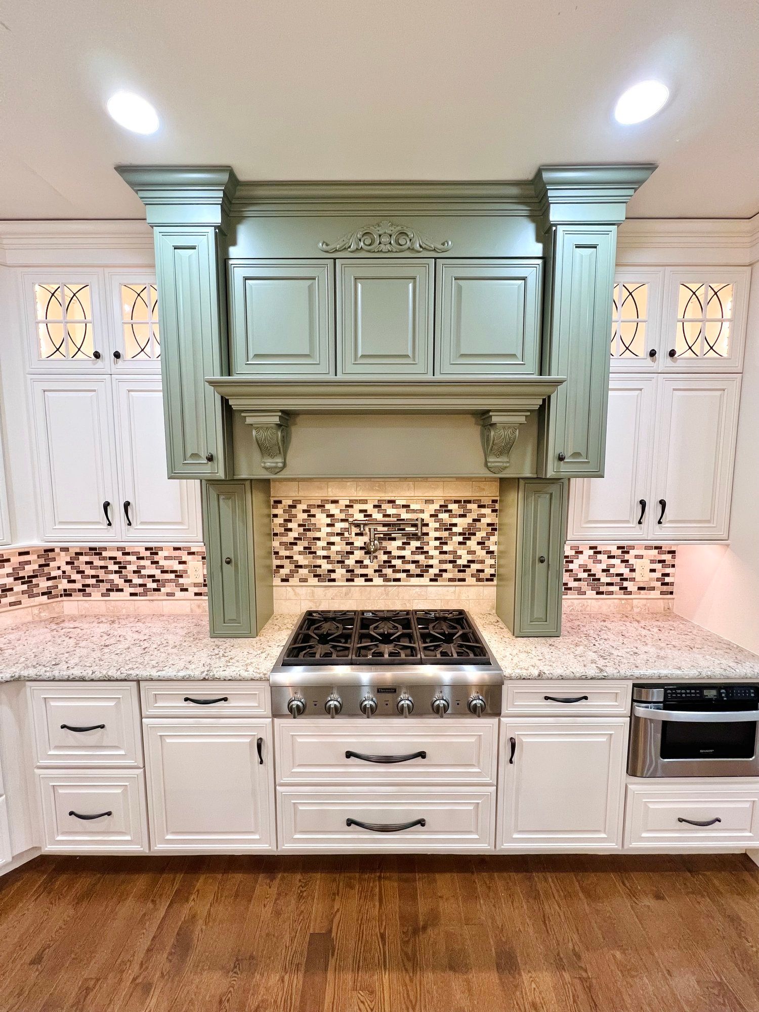 Kitchen with white cabinets, green range hood, granite countertops, and stainless steel appliances.
