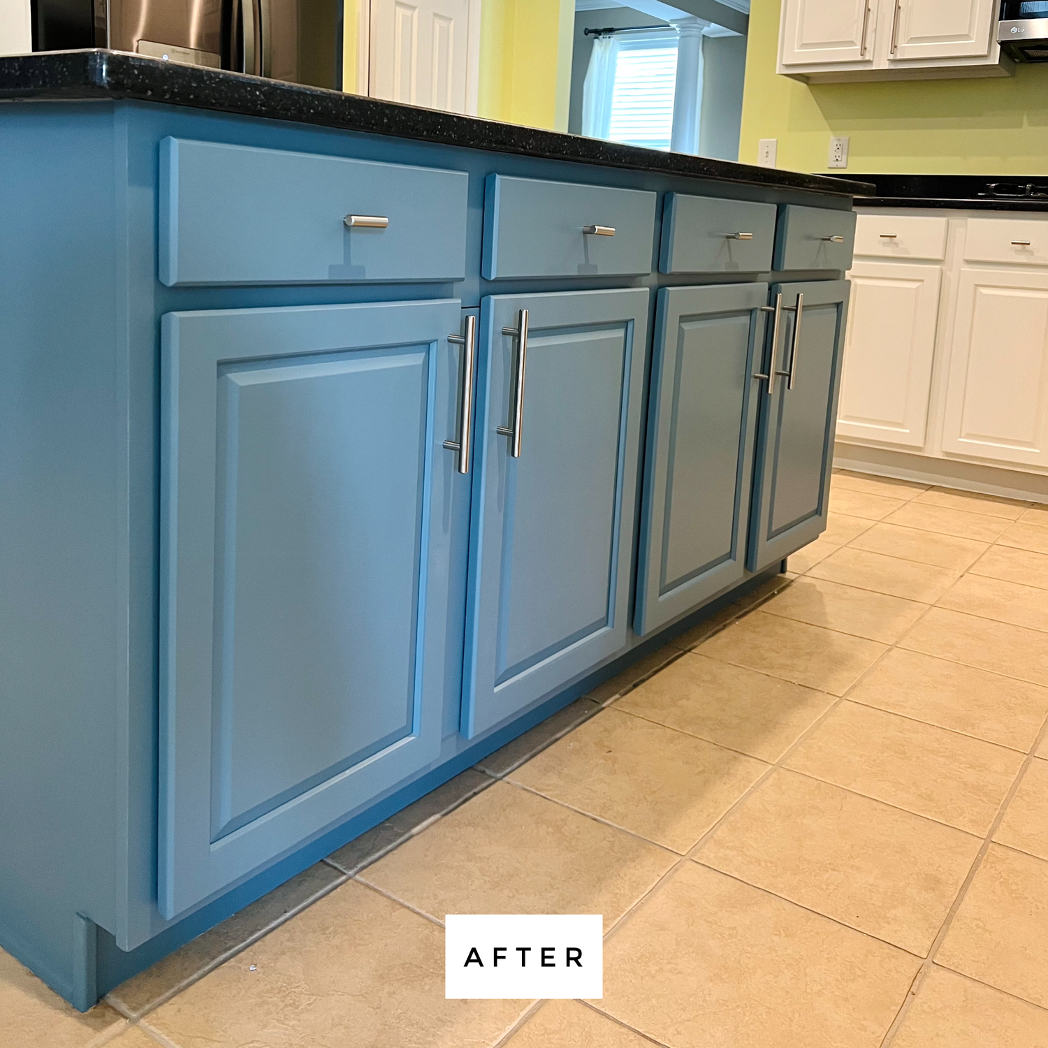Blue kitchen island with black countertop, silver handles, and white cabinets in the background.
