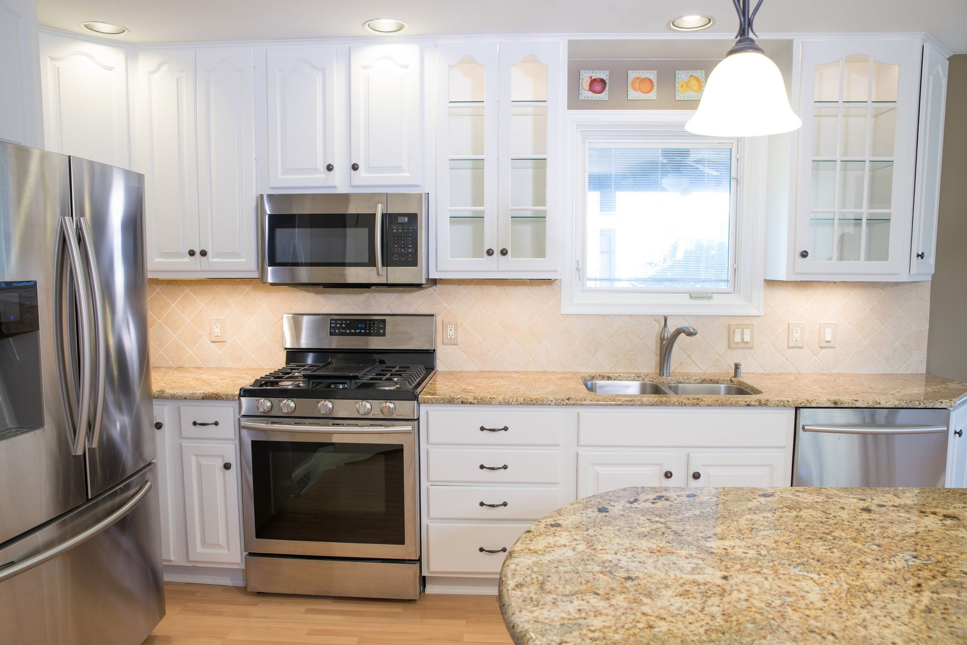 White kitchen with stainless steel appliances, granite countertops, and overhead lighting.