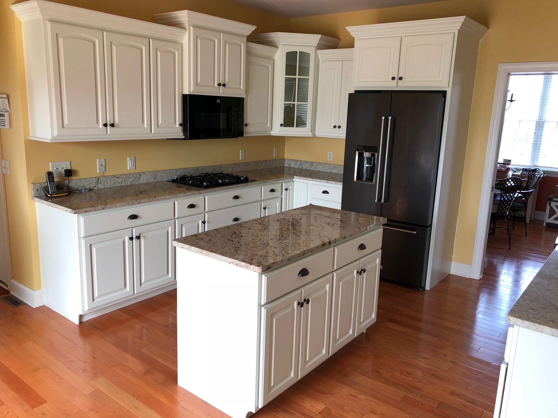 Kitchen with white cabinets, granite countertops, stainless steel fridge, and wooden floor.