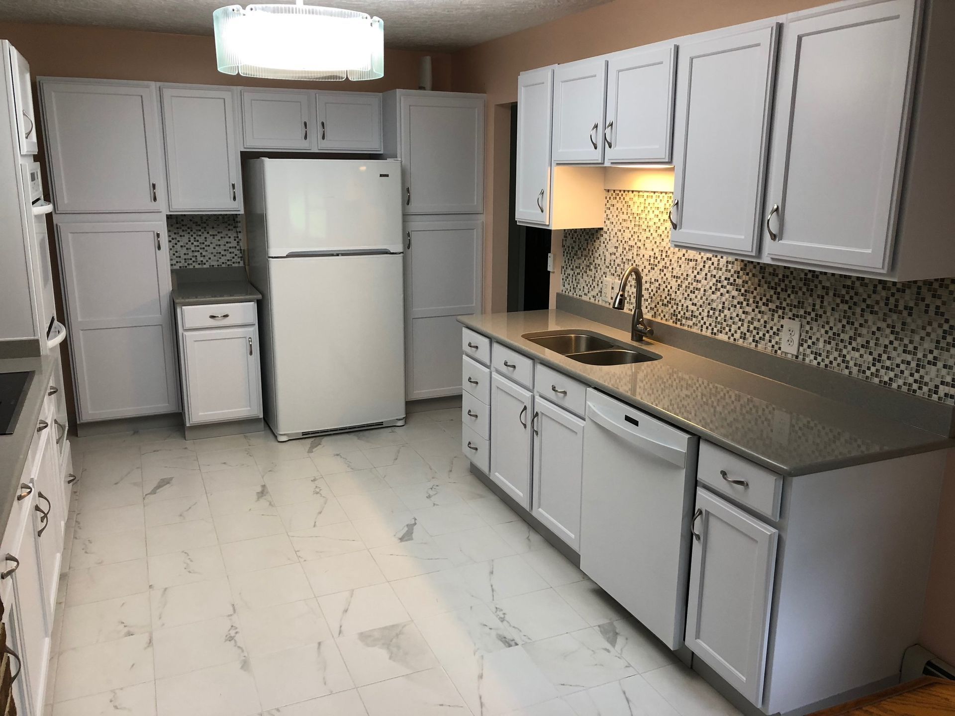 White kitchen with white cabinets, refrigerator, and countertop. Dark tile backsplash and light floor.