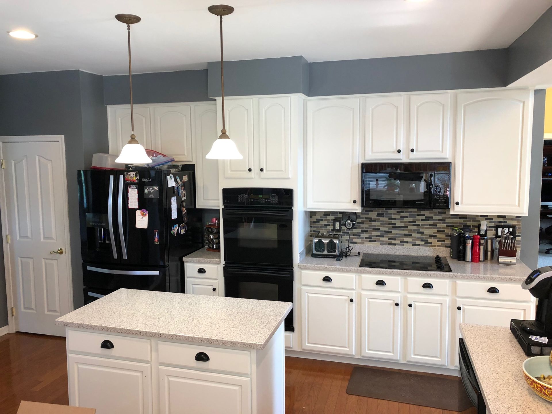 White kitchen with dark appliances, island, and gray wall.