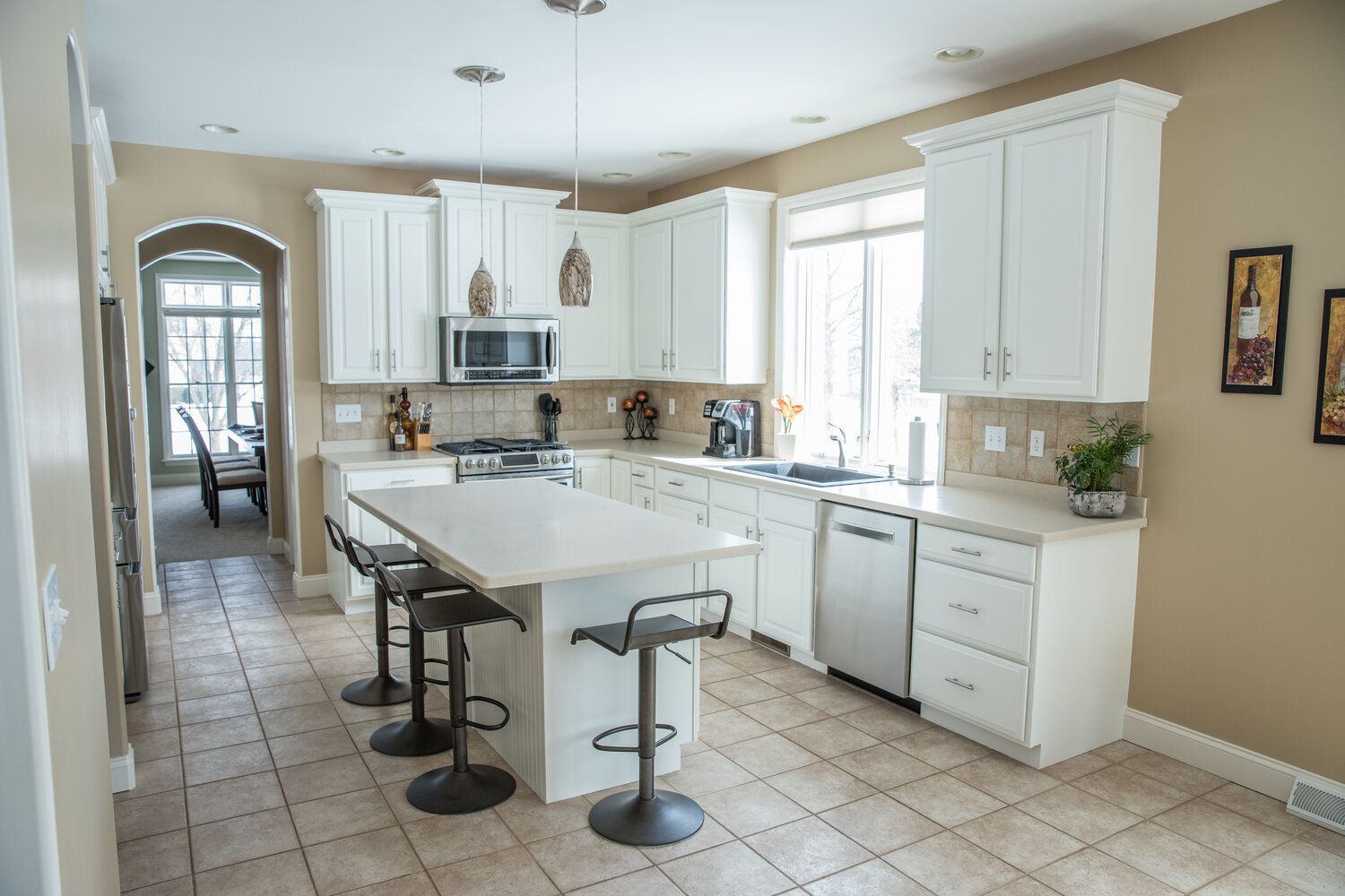 Bright kitchen with white cabinets, island with stools, and beige walls.