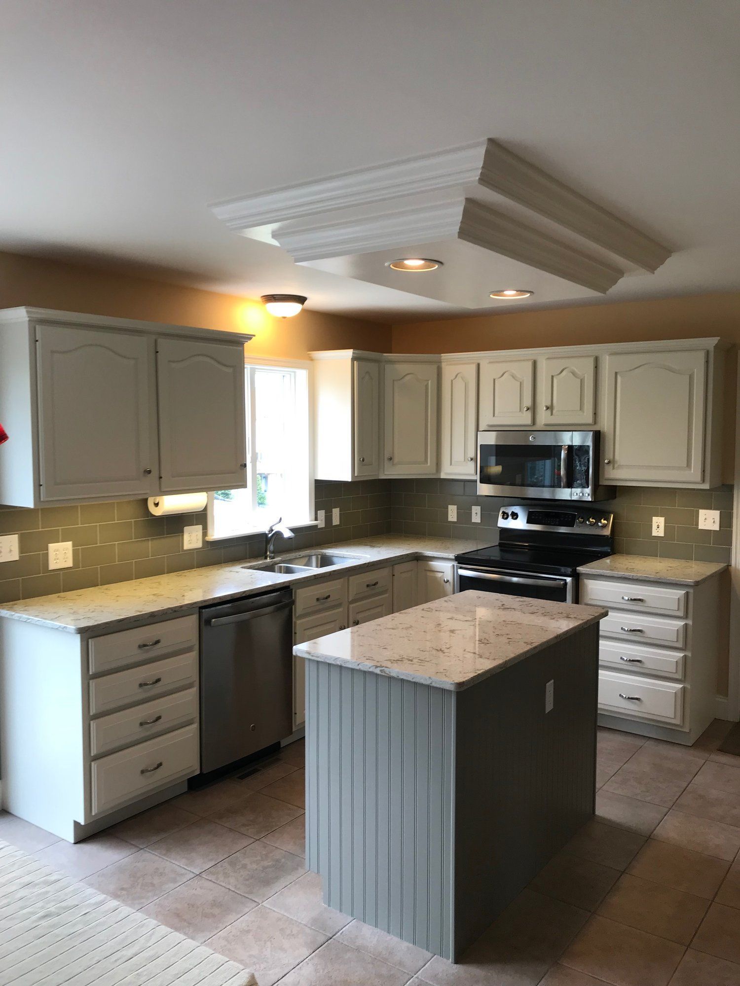 Kitchen with light gray cabinets, island, and appliances; light-colored countertops and backsplash.