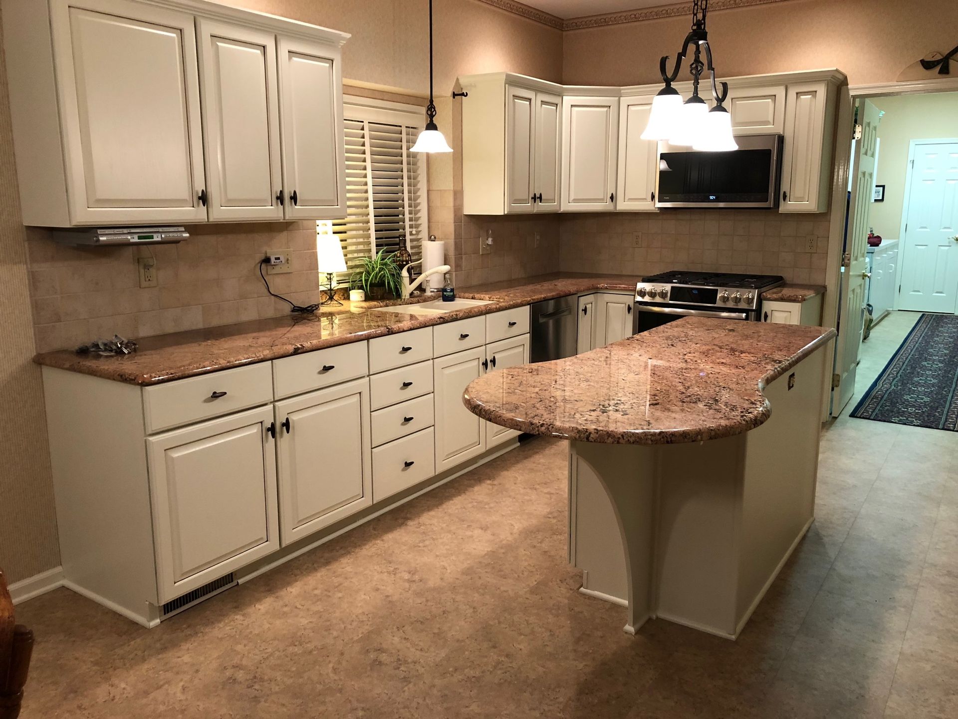 Cream-colored kitchen with granite countertops. Cabinets, island, and appliances.