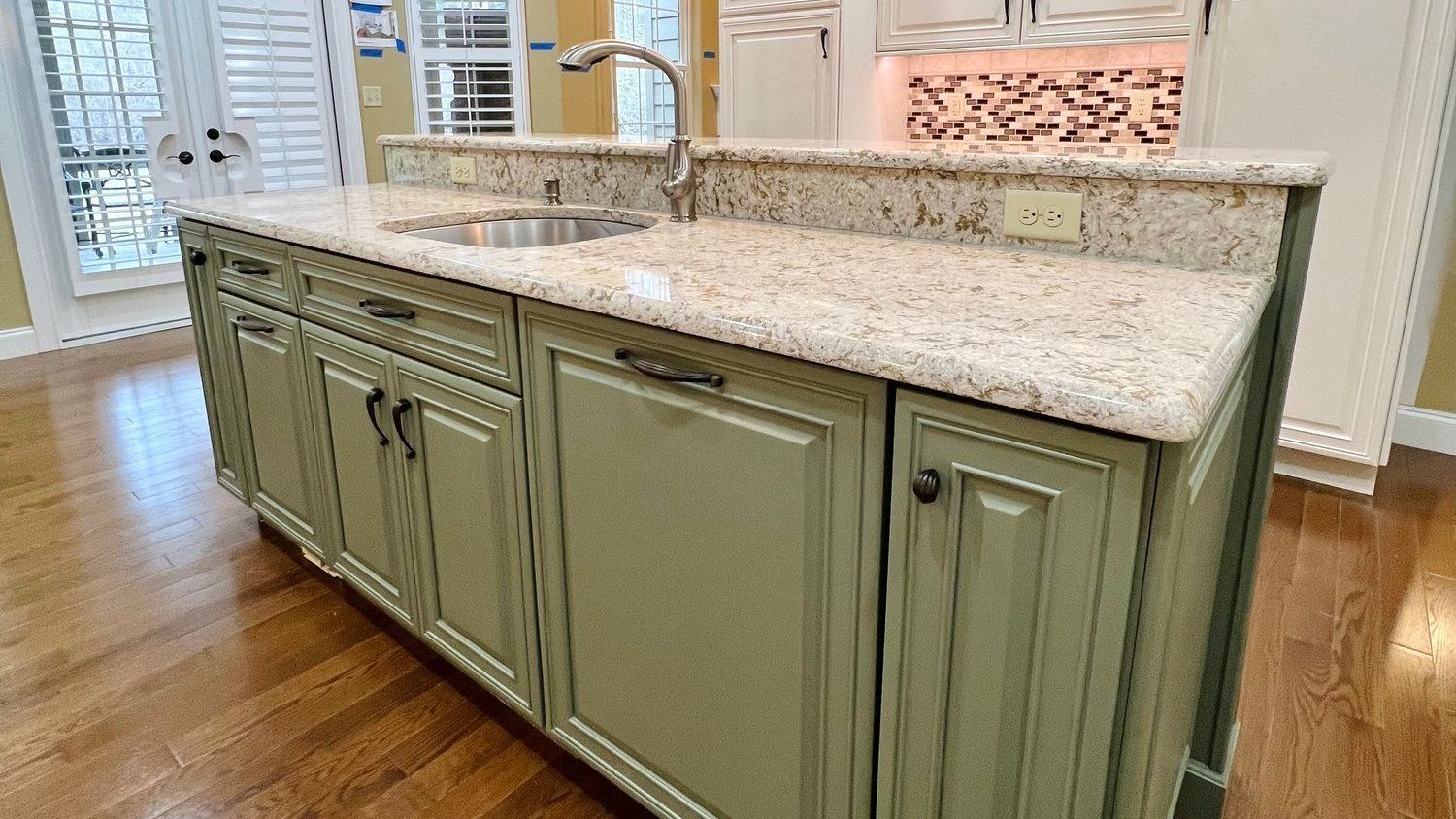 Sage green kitchen island with granite countertop, sink, and wooden floor.