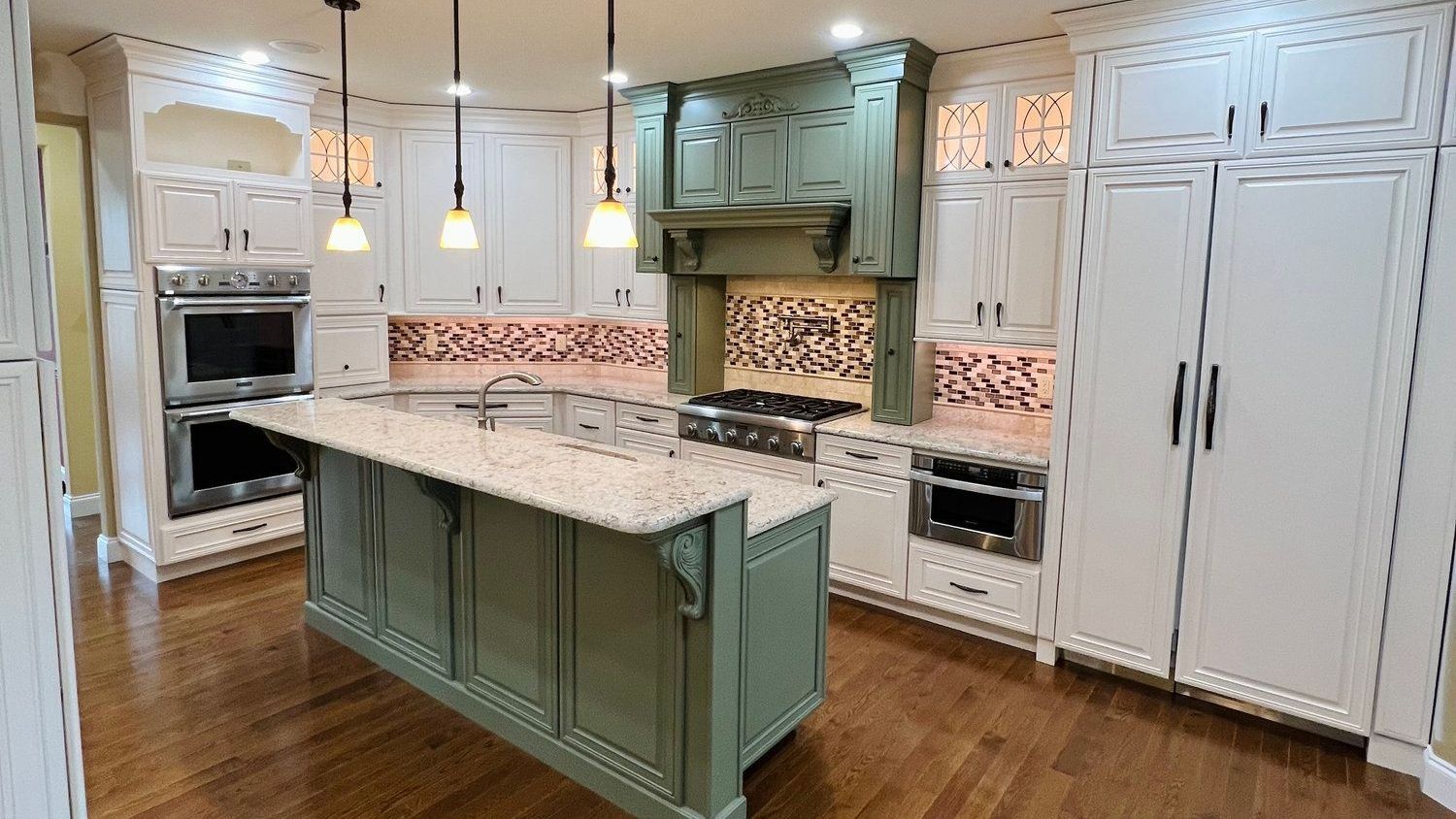 Spacious kitchen with white and sage green cabinets, island, stainless steel appliances, and tile backsplash.