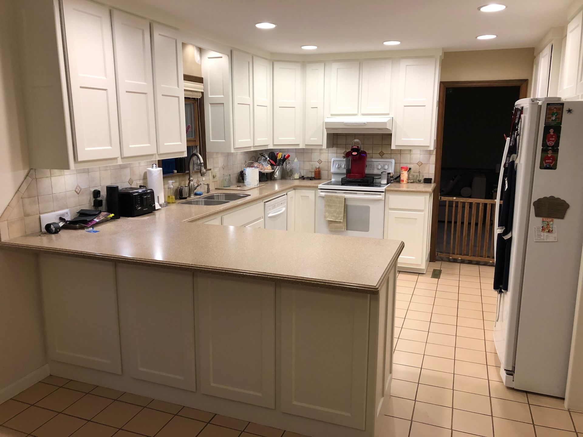 Cream-colored kitchen with white cabinets, light countertops, stove, refrigerator, and tile floor.