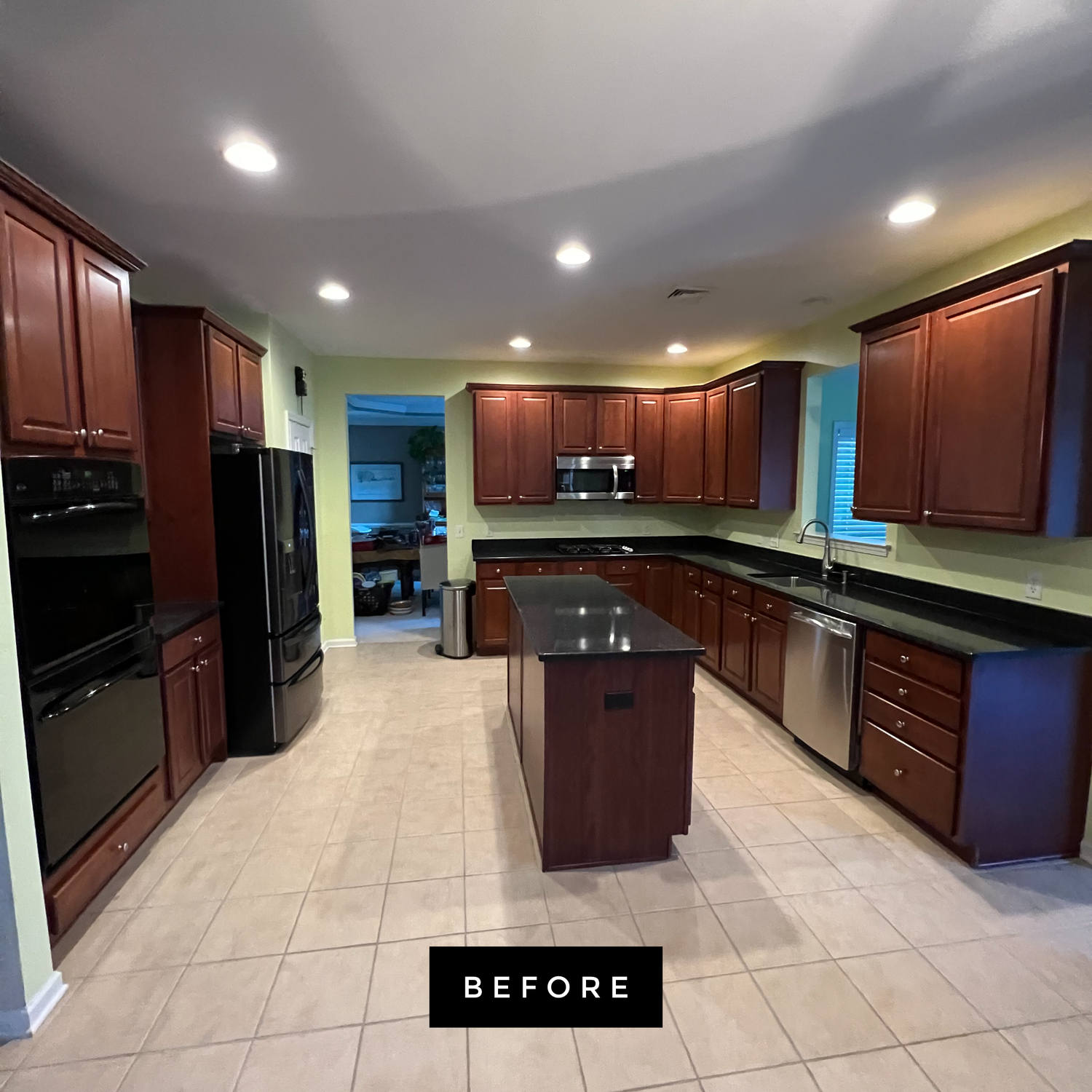 Kitchen with dark cabinets, black appliances, and island; light-colored tile floor. 