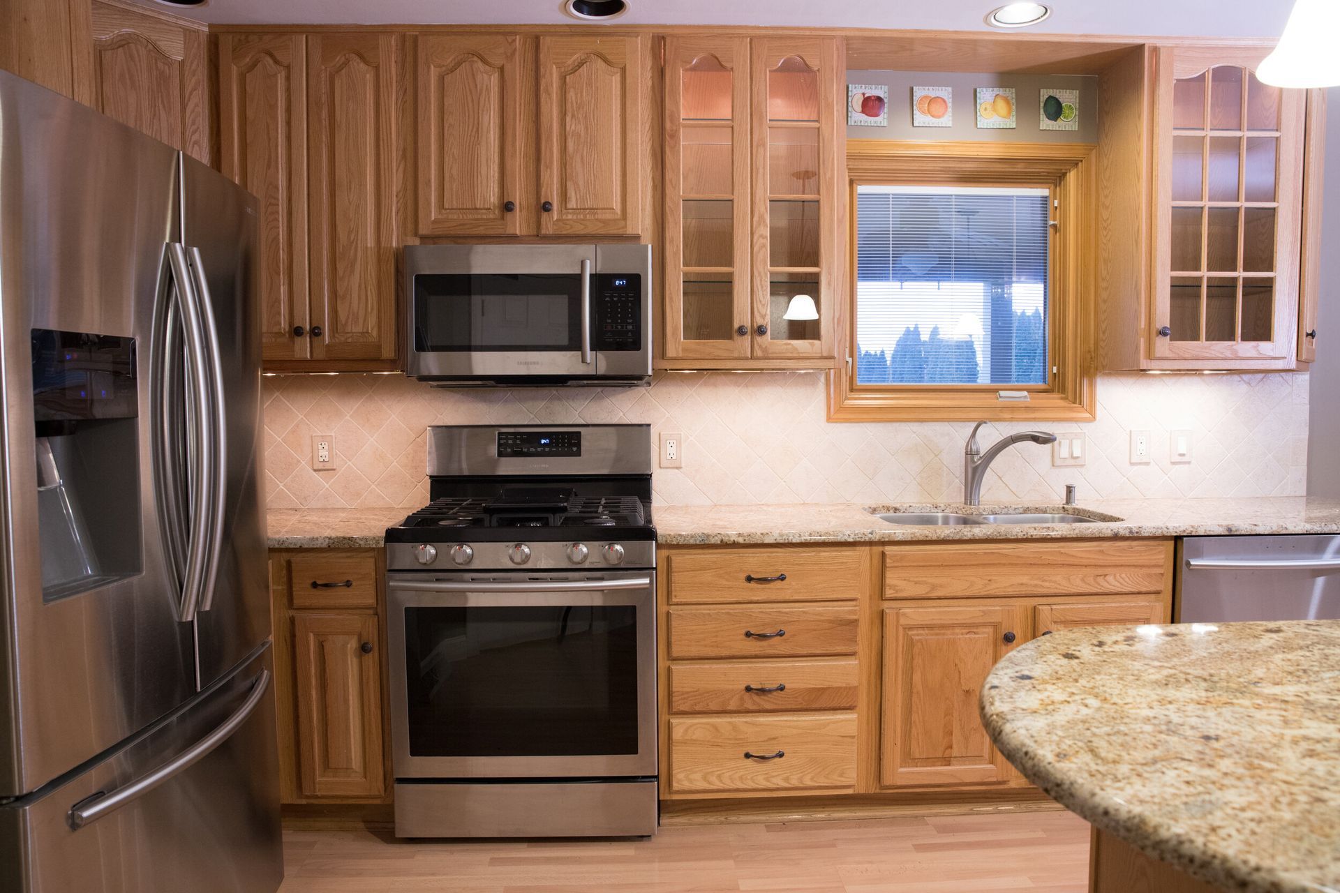 Kitchen with light wood cabinets, stainless steel appliances, granite countertops, and a window.