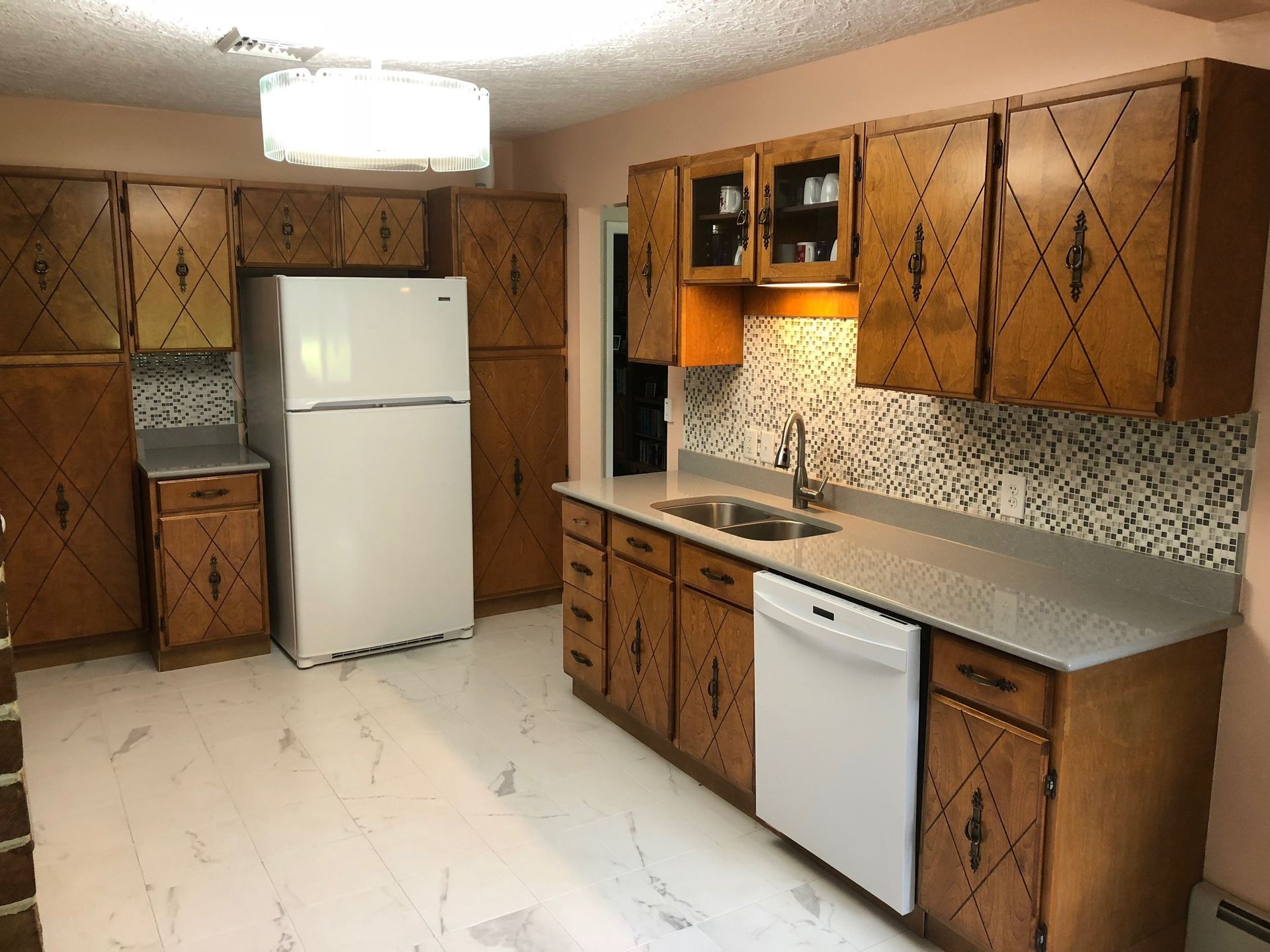 Kitchen with wooden cabinets, white appliances, and light countertops. The backsplash has a speckled pattern and the floor is white.