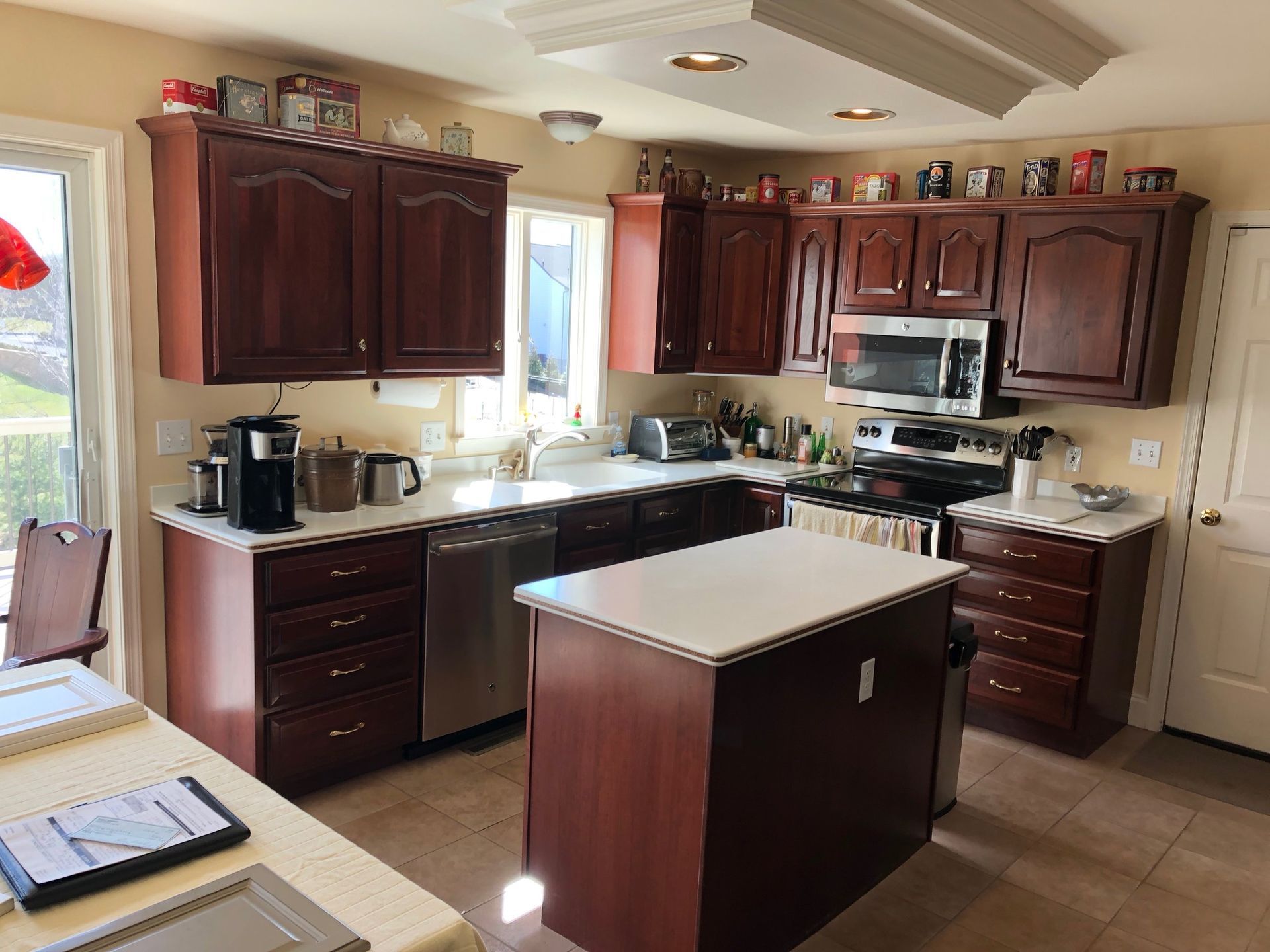 A kitchen with dark wood cabinets, stainless steel appliances, a white island, and light-colored countertops.