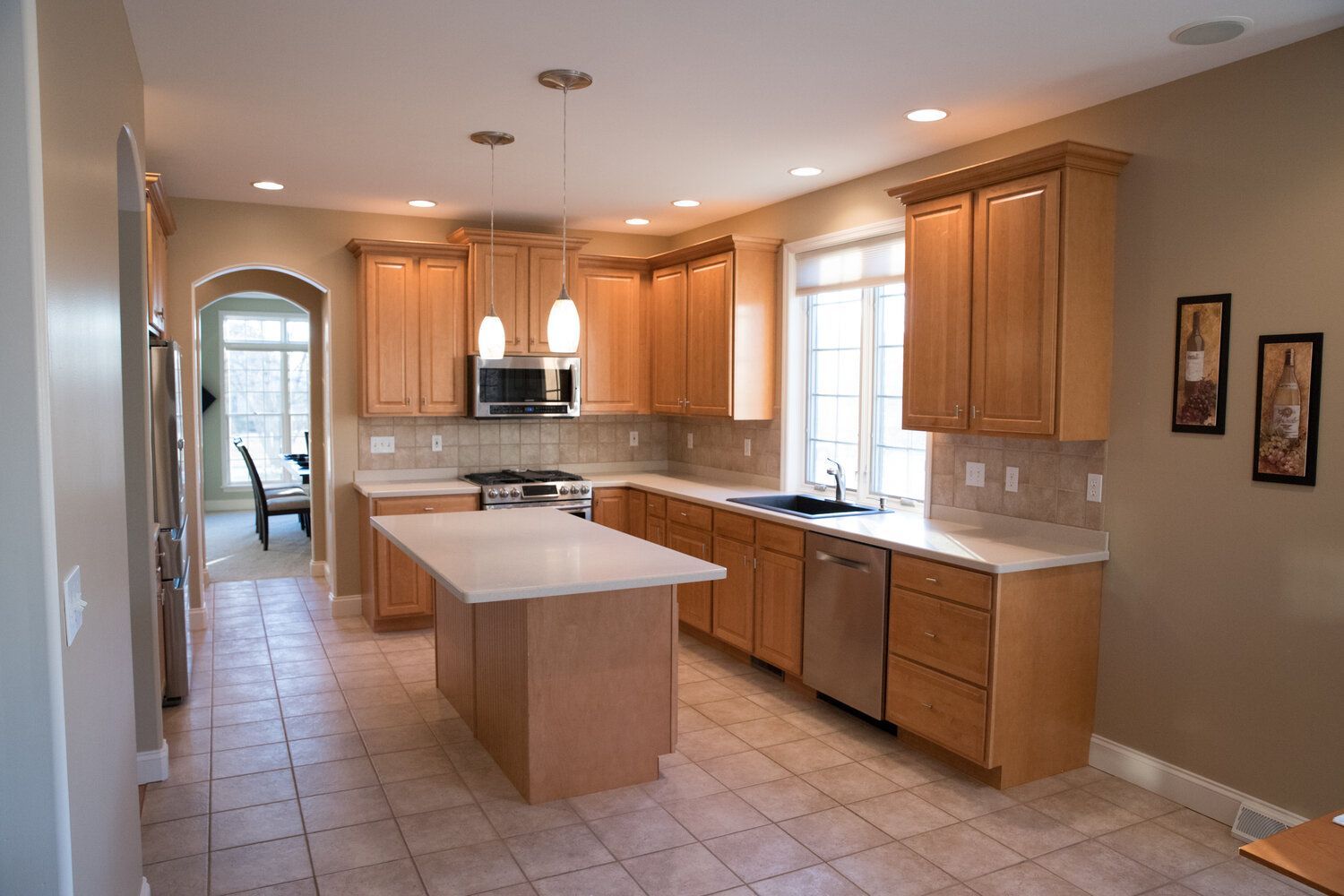Beige kitchen with light wood cabinets, island, stainless steel appliances, and tile flooring.