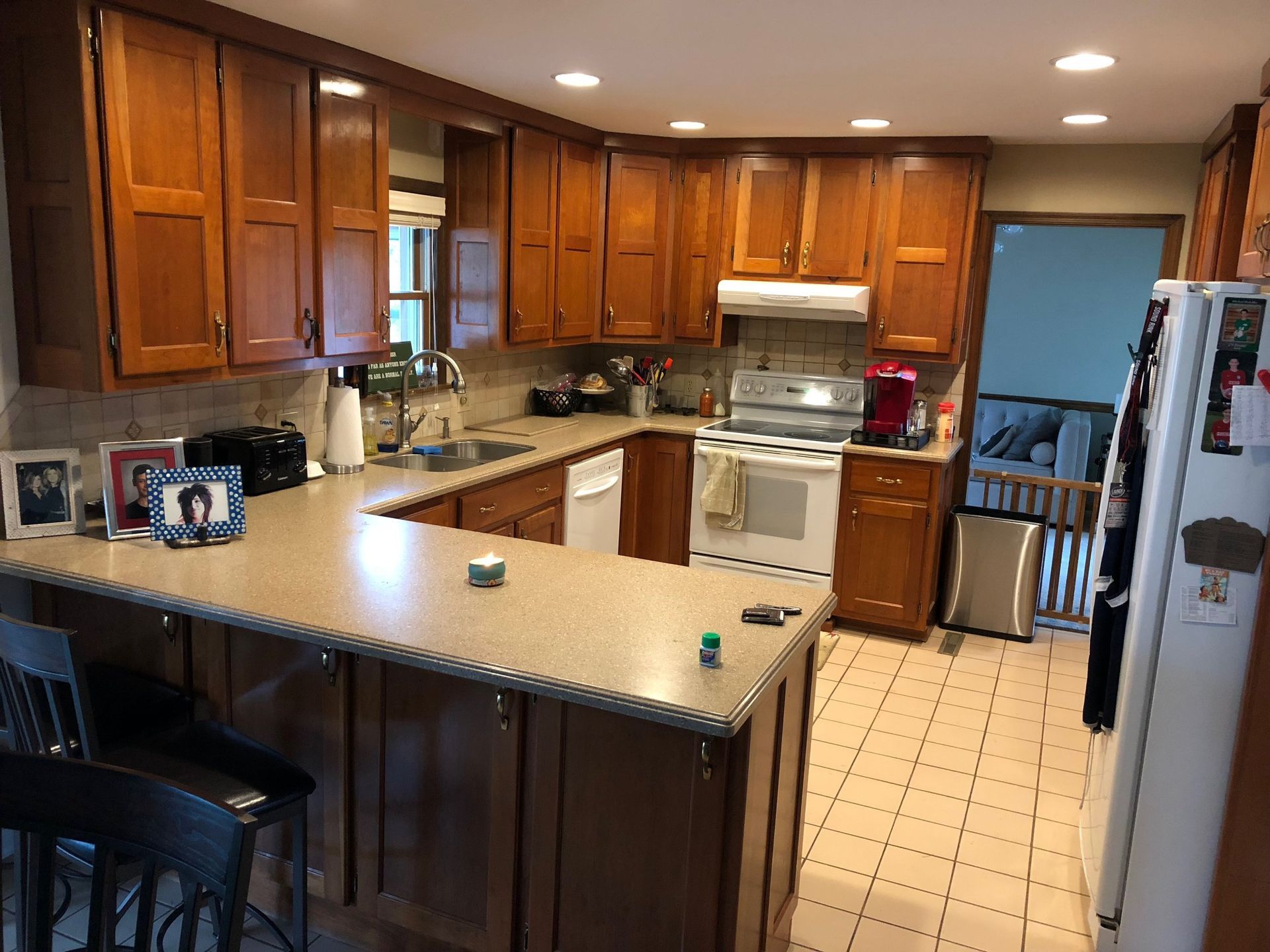 U-shaped kitchen with brown cabinets, tan countertops, and stainless steel appliances. Bar stools sit at the peninsula.