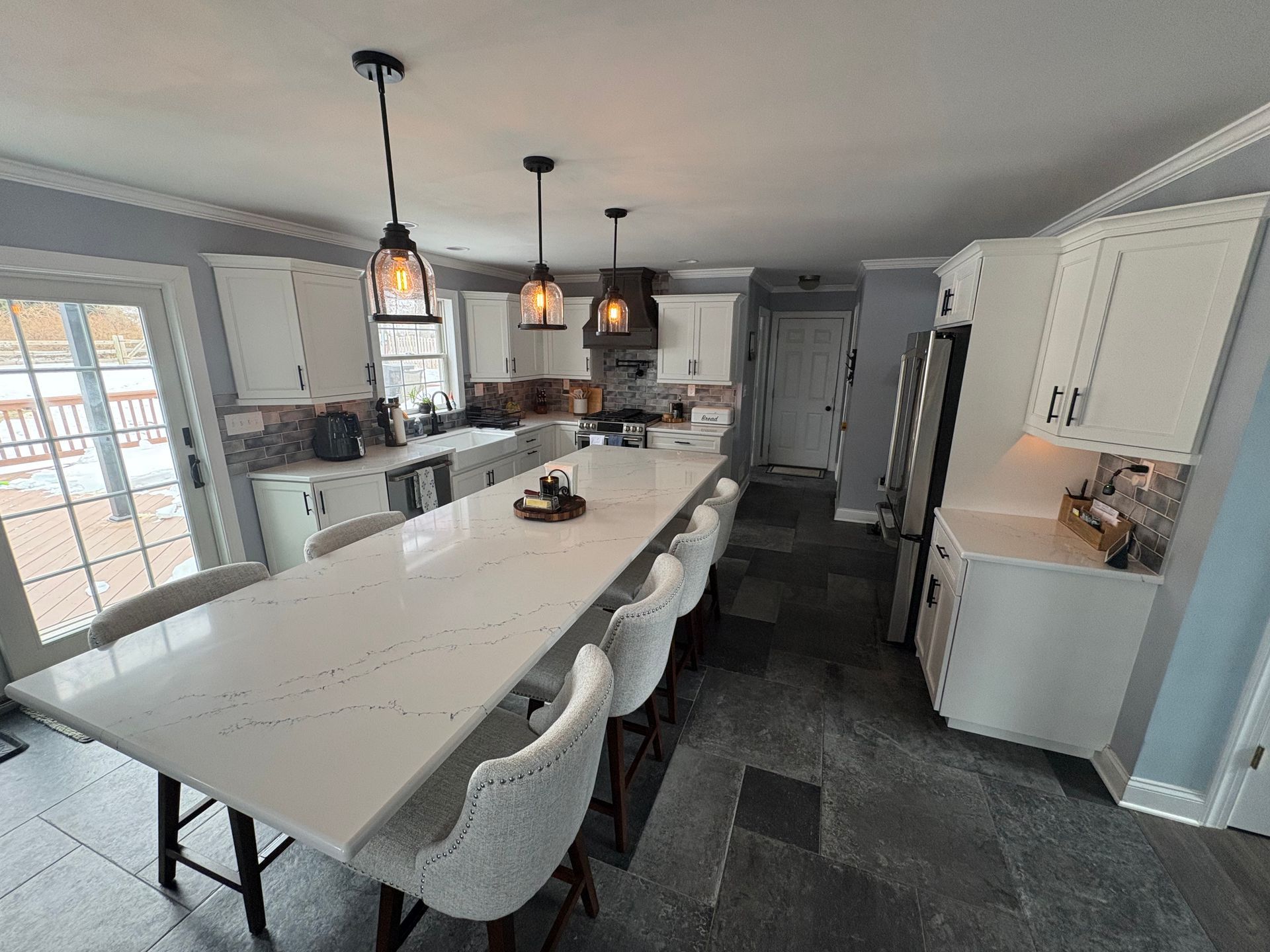 Modern kitchen with a large white island, pendant lights, bar stools, and gray tile flooring