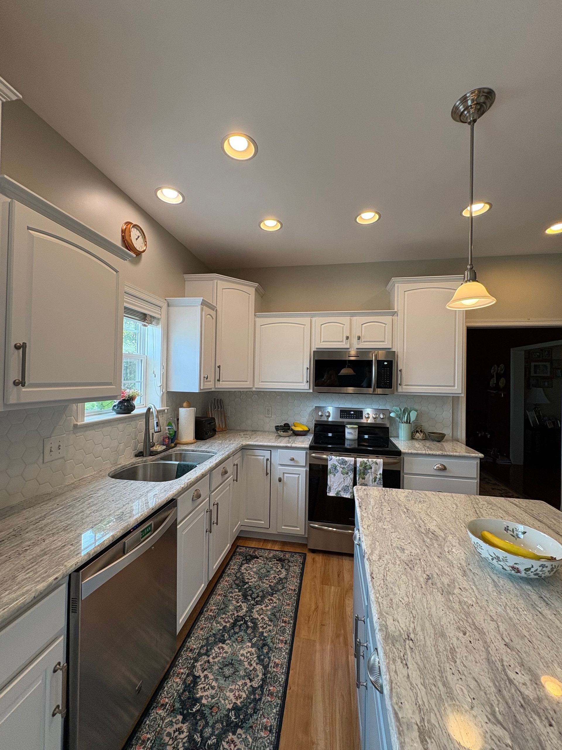 White kitchen with granite countertops and stainless steel appliances; a rug runs lengthwise.