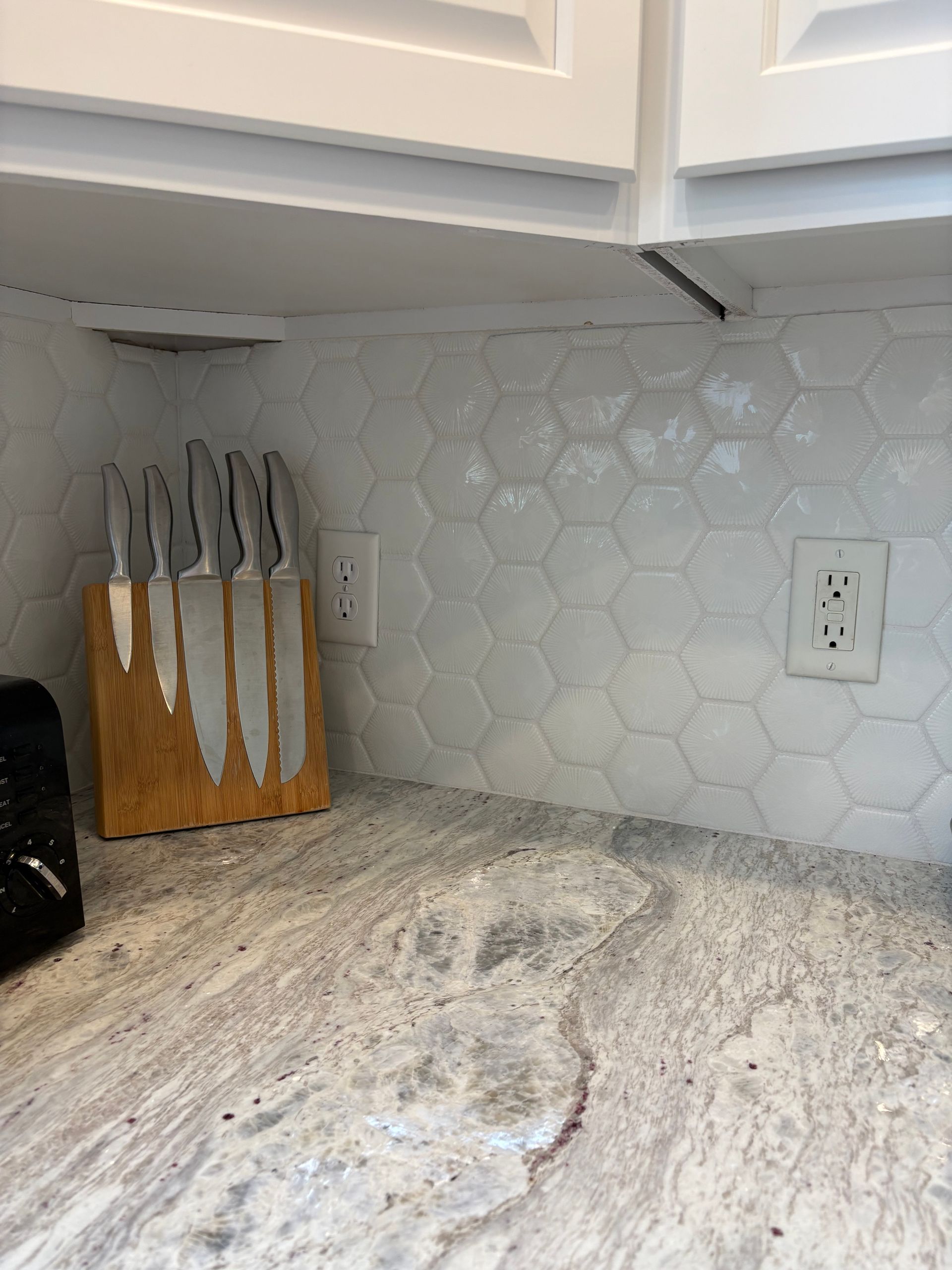Kitchen counter with a knife block, outlets, and hexagonal white backsplash.
