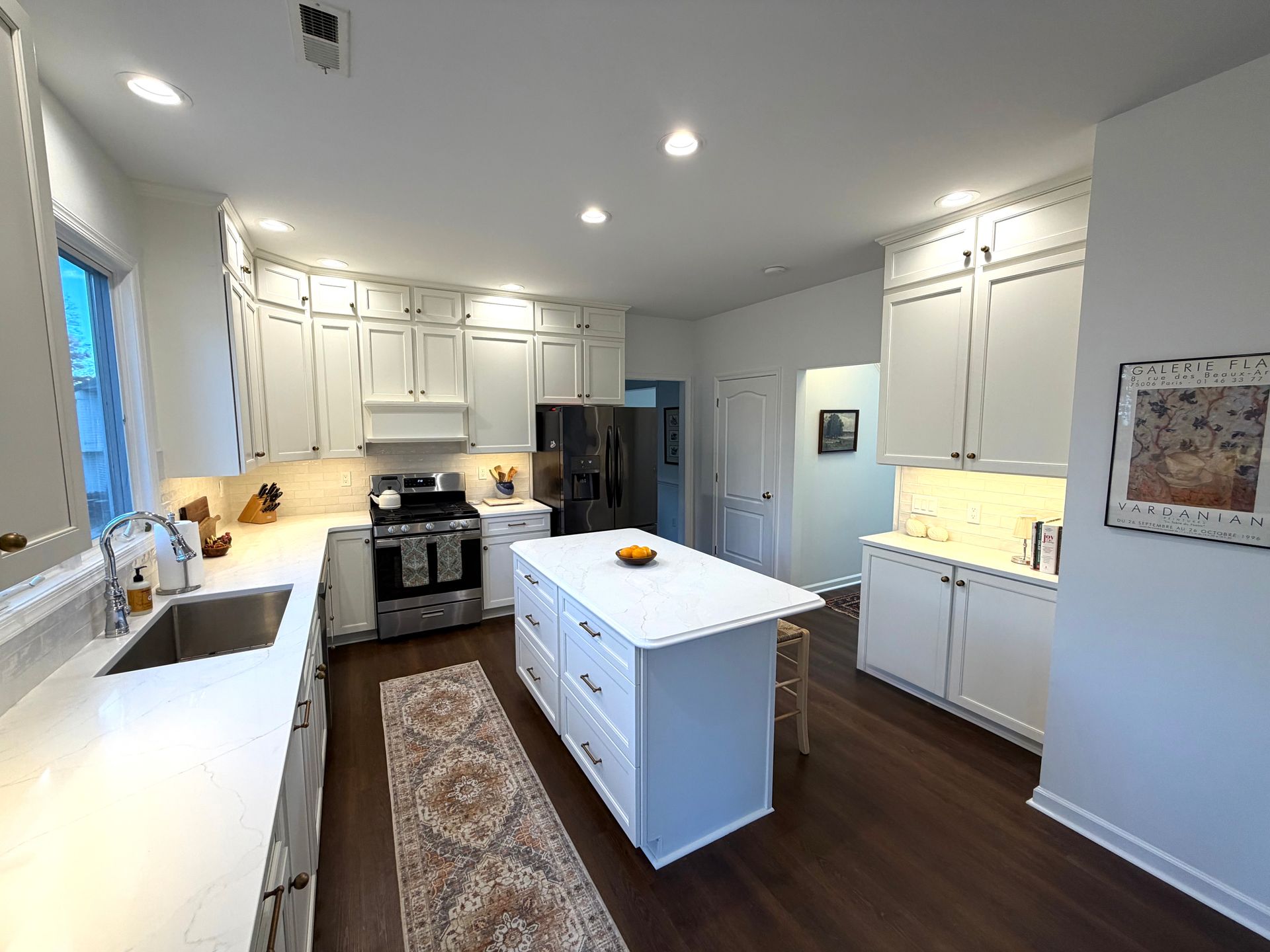 White kitchen with island, cabinets, dark wood floor, stainless steel appliances, and a small rug.