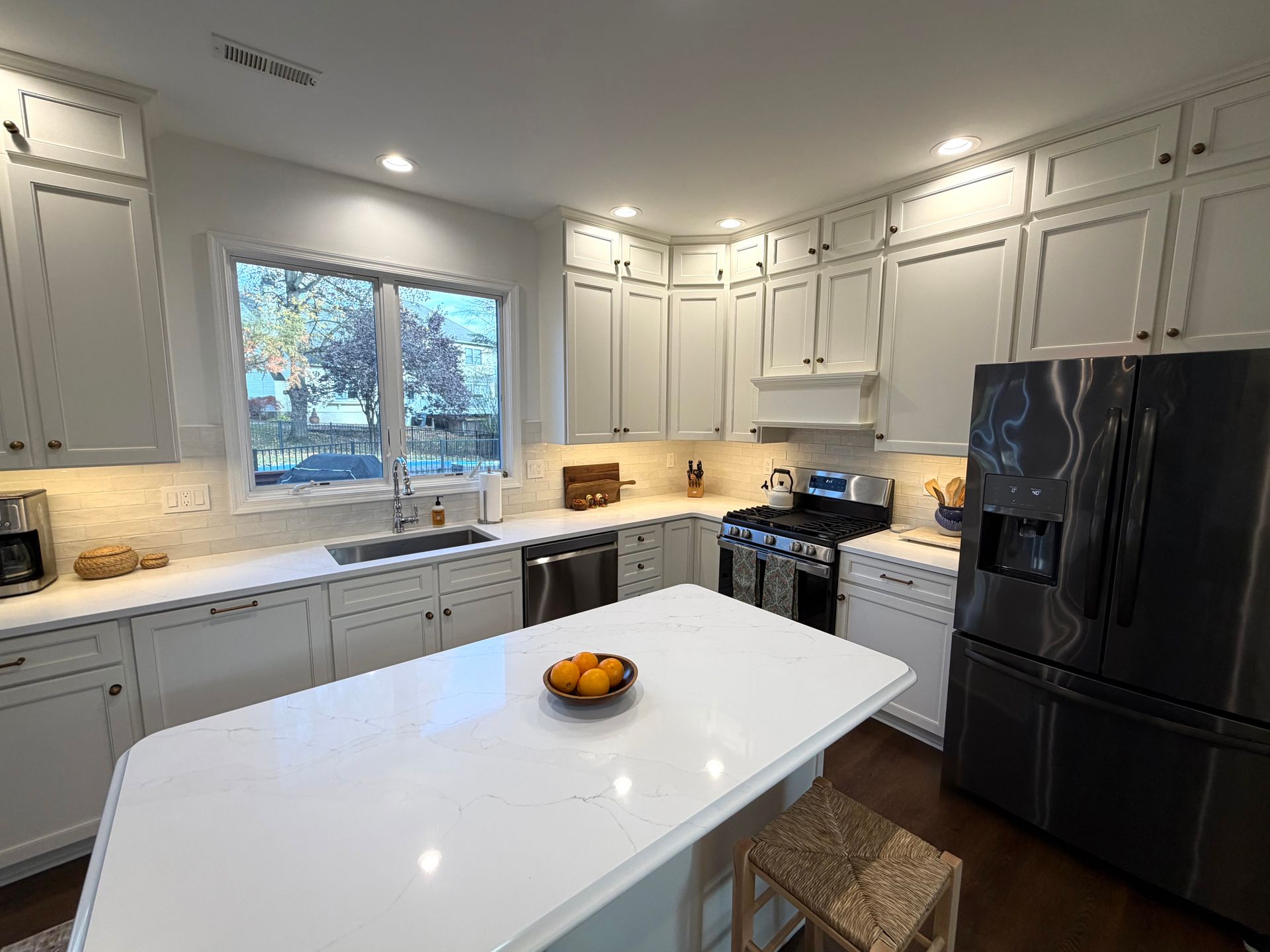 White kitchen with island, stainless steel appliances, and window with outdoor view.