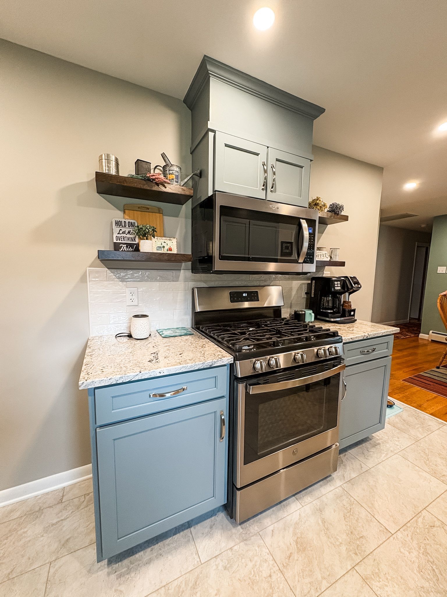 Blue kitchen cabinets with stainless steel appliances, shelves, and a microwave.