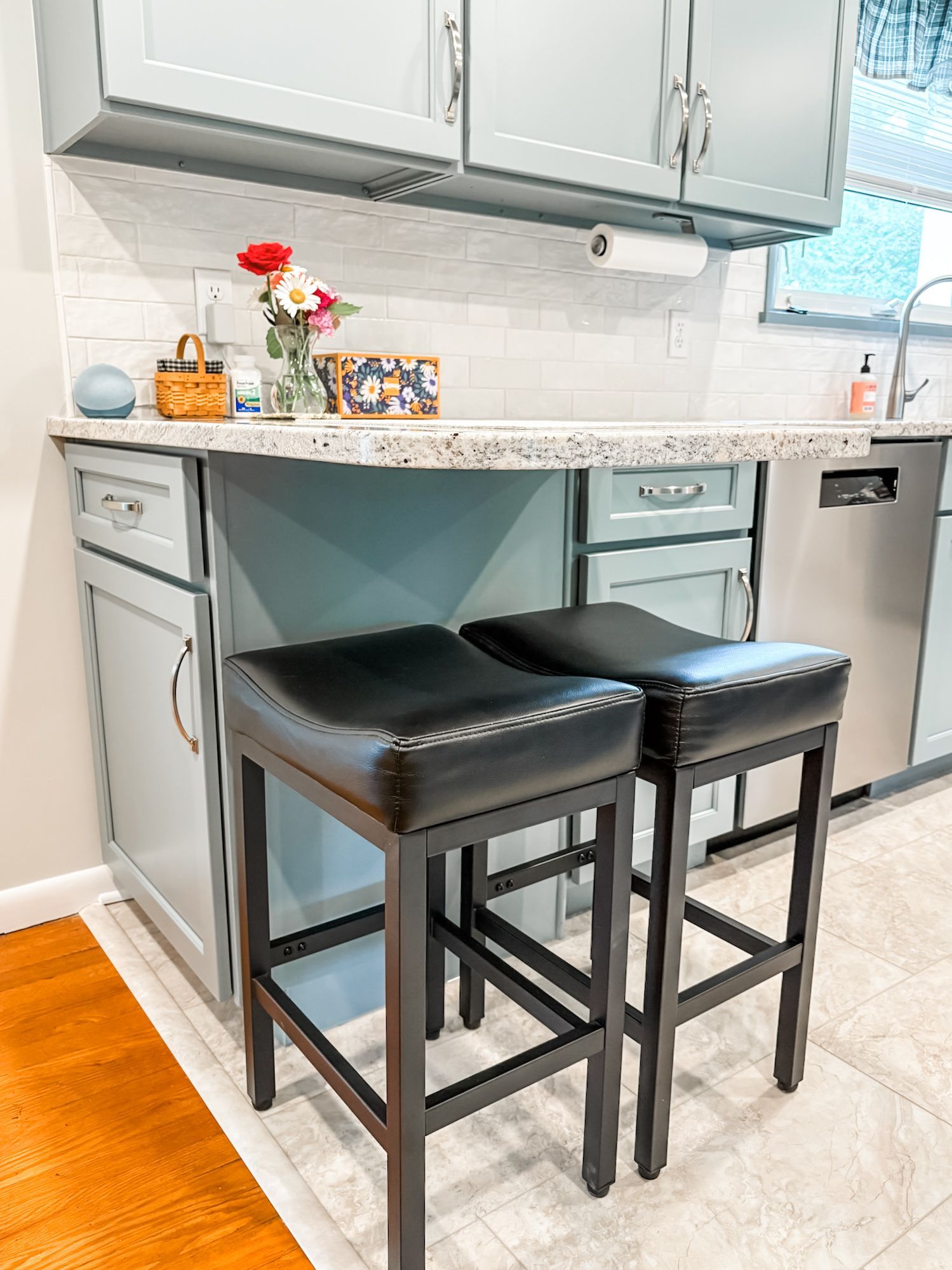 Two black bar stools at a blue kitchen island. Cabinets, countertop, and flowers are also visible.