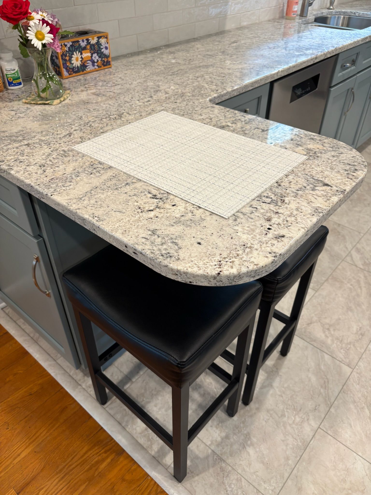 Kitchen island with granite countertop, two black stools, and gray cabinets.