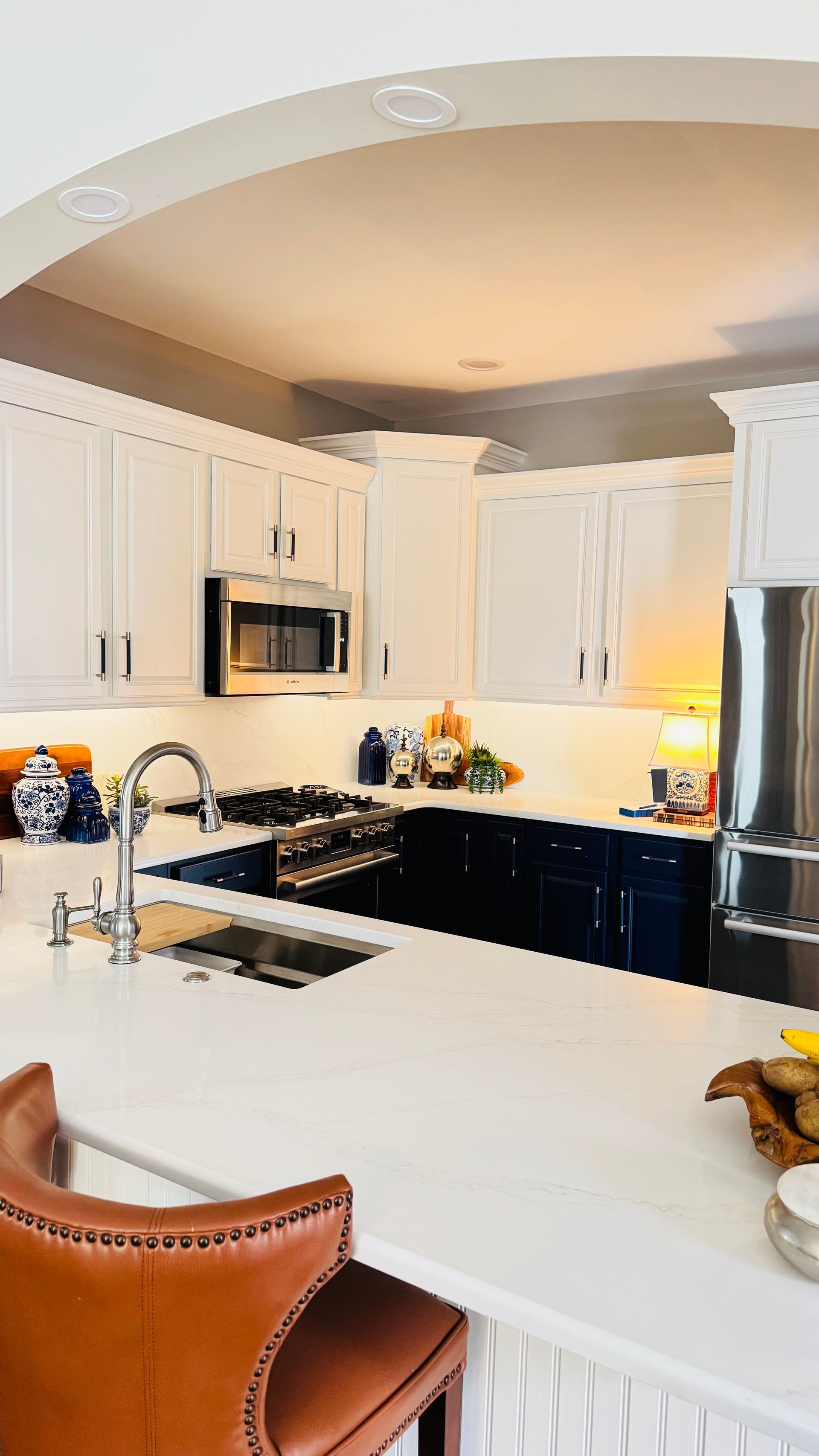 Kitchen with white cabinets, navy island, stainless steel appliances, and brown leather stool.